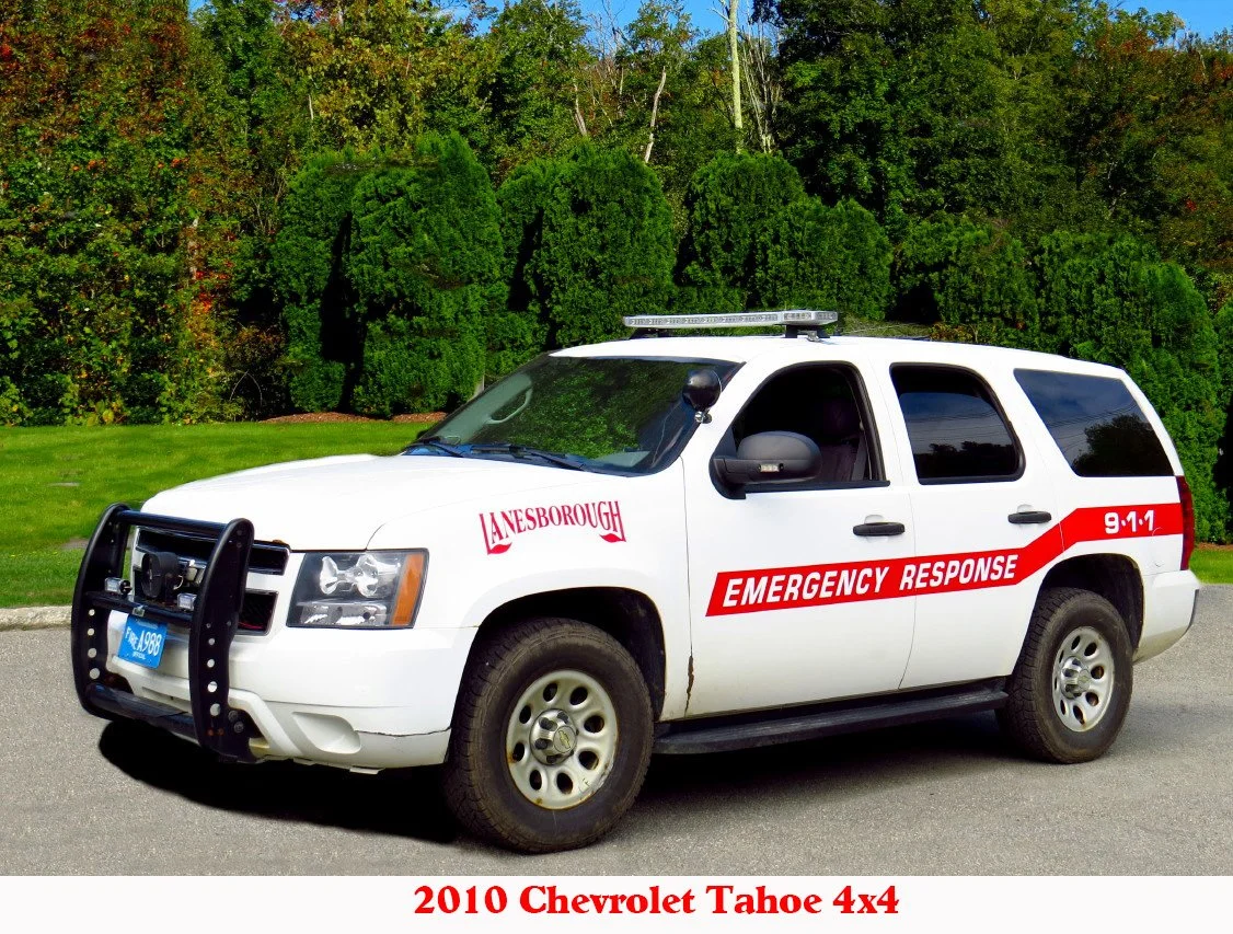 A 2010 Chevrolet Tahoe 4x4 used as an emergency response vehicle, parked on a street with green trees in the background.