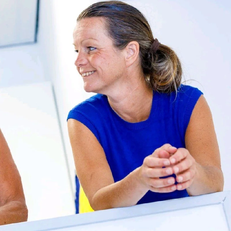 Close-up of a man with short light-colored hair, wearing a dark suit and tie, against a plain white background.