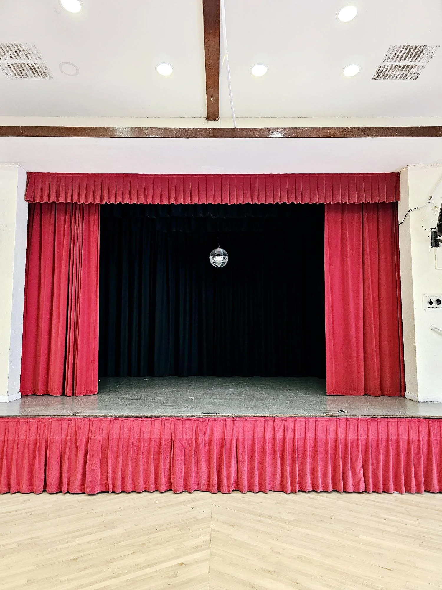 Empty stage with red curtains and a black backdrop, with a small disco ball hanging from the ceiling.