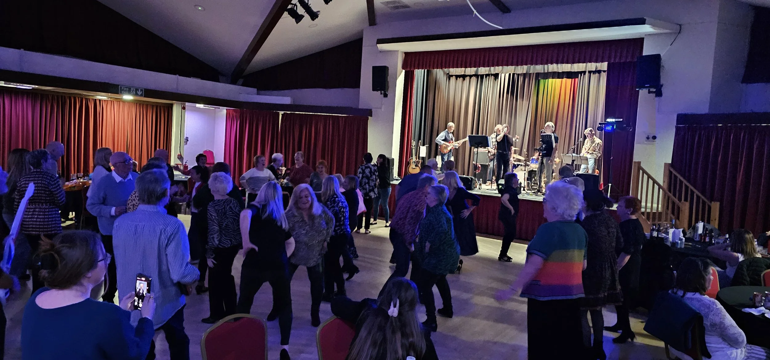 People dancing and socializing in a hall with a live band performing on stage.