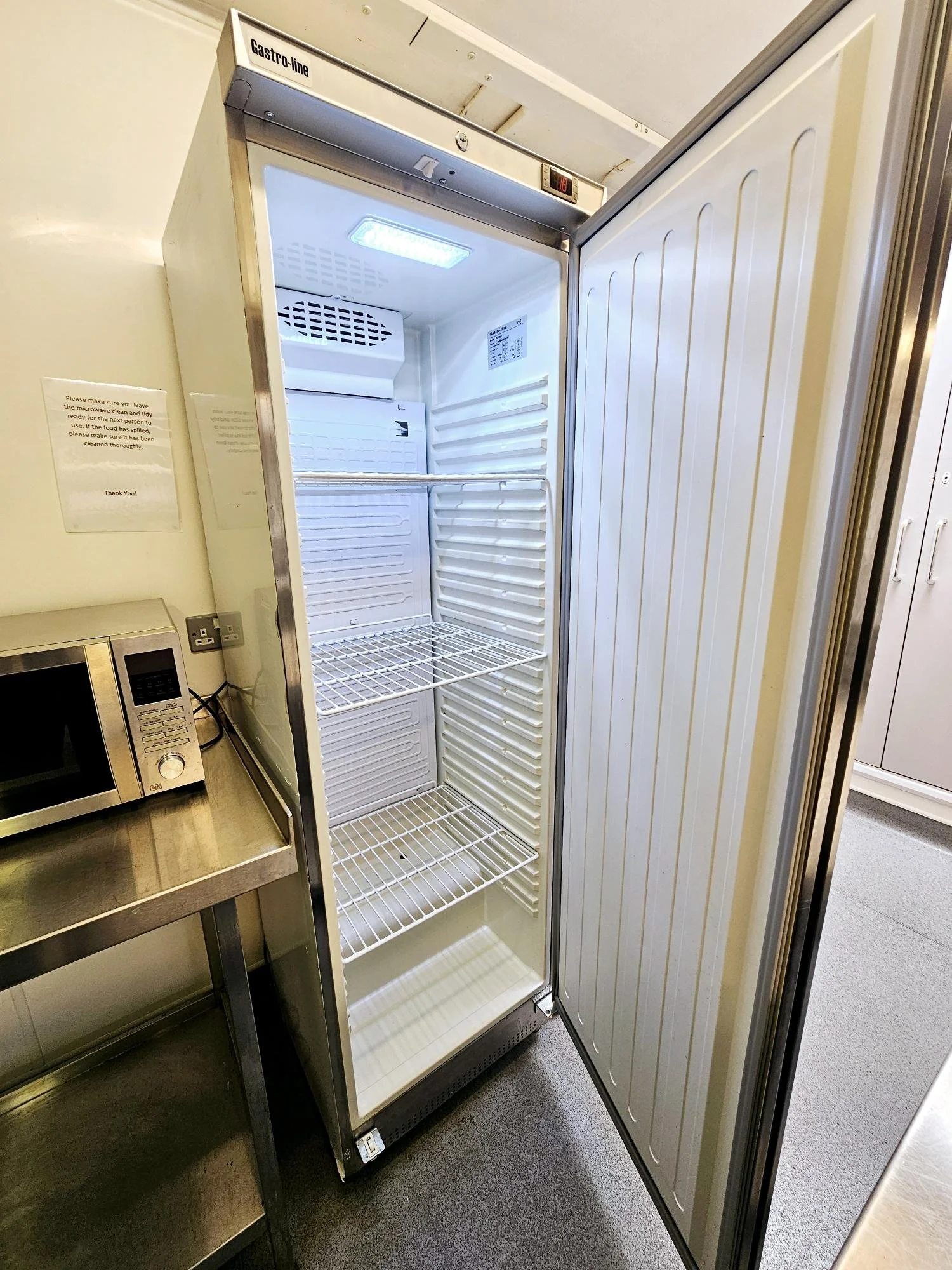 Empty commercial refrigerator with open door, metal shelves, and interior light