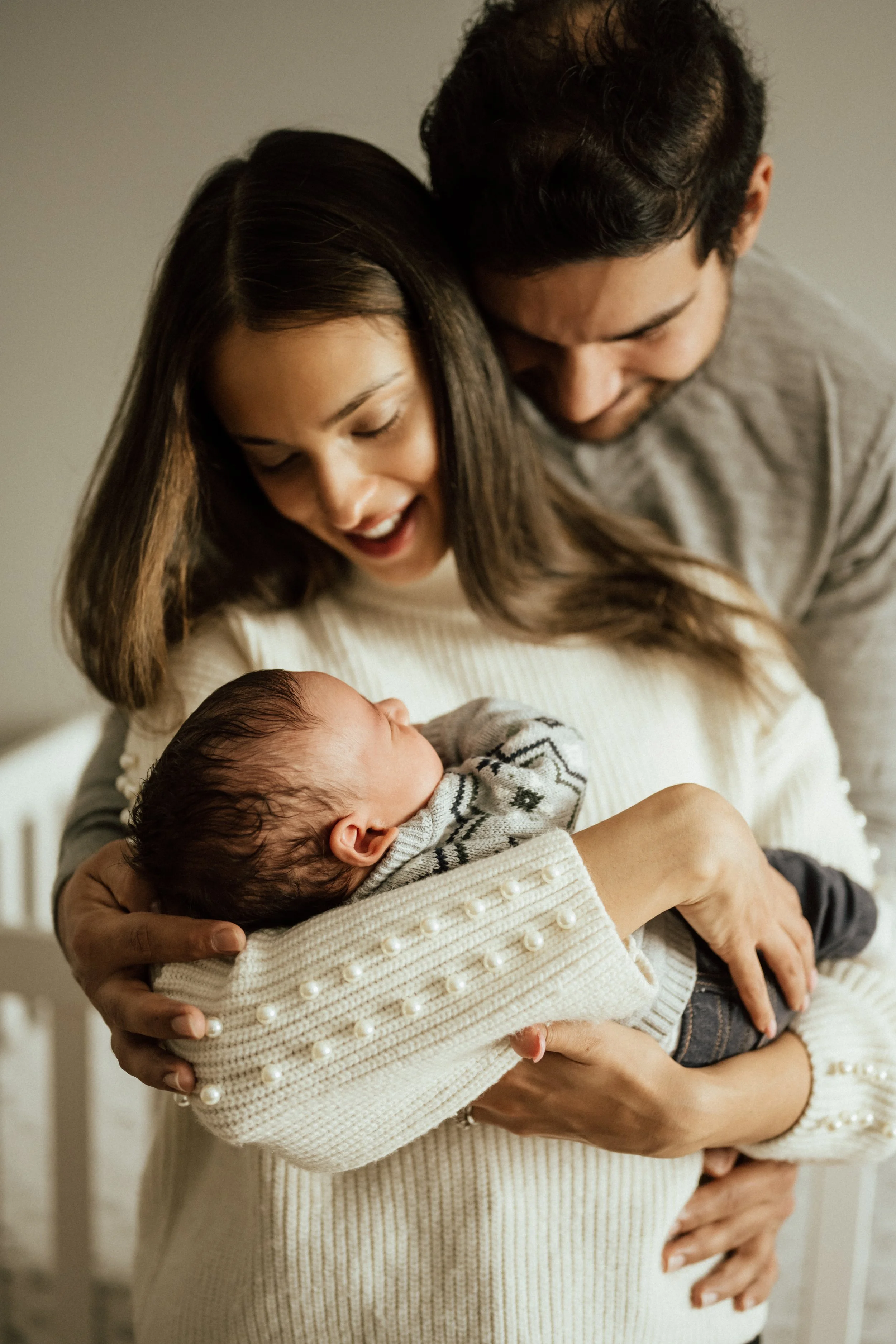 A couple is holding and looking at a newborn baby indoors.
