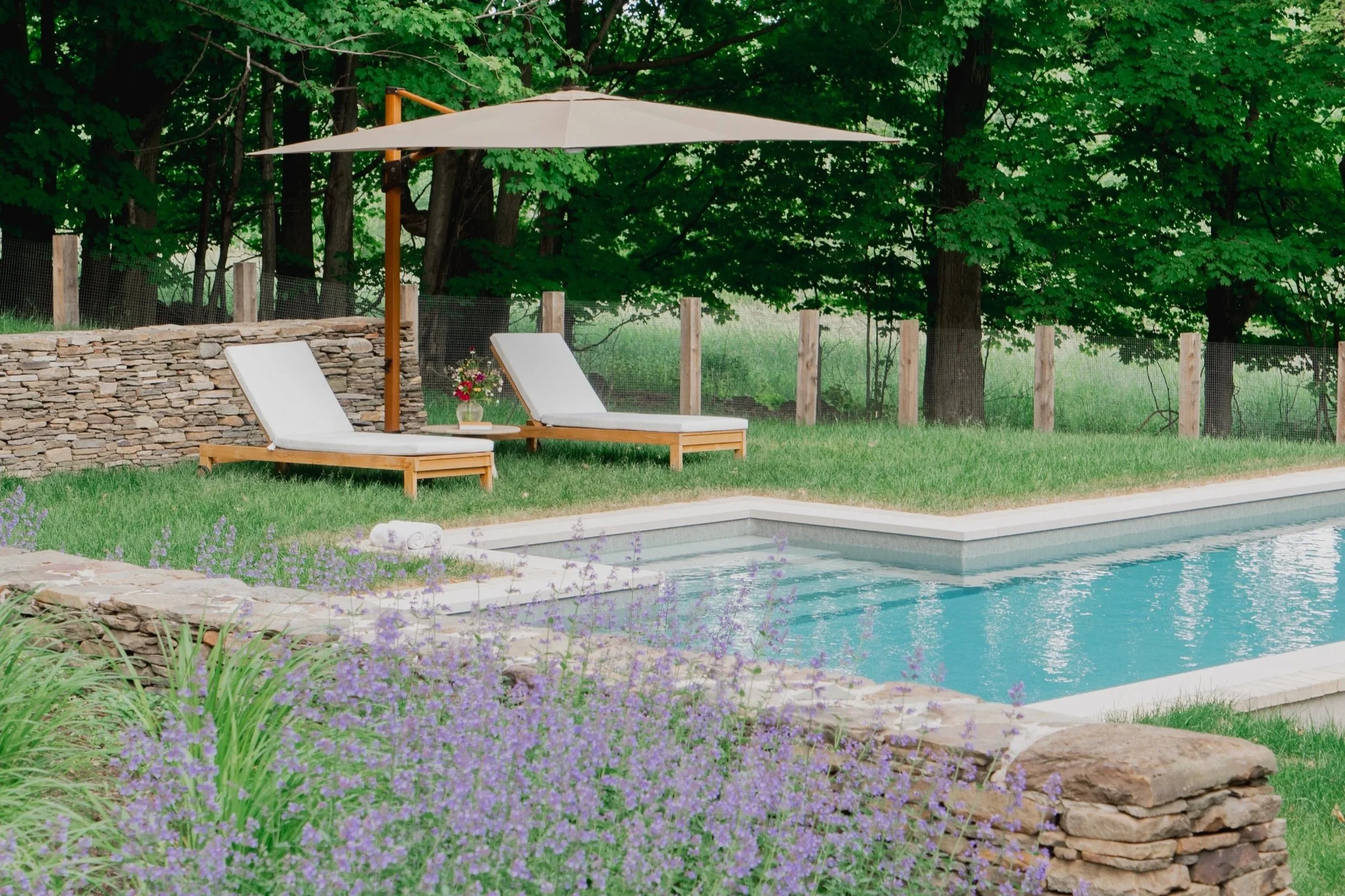 Piscine moderne en campagne bordée de murs de pierre naturelle et d'une clôture sur mesure en bois
