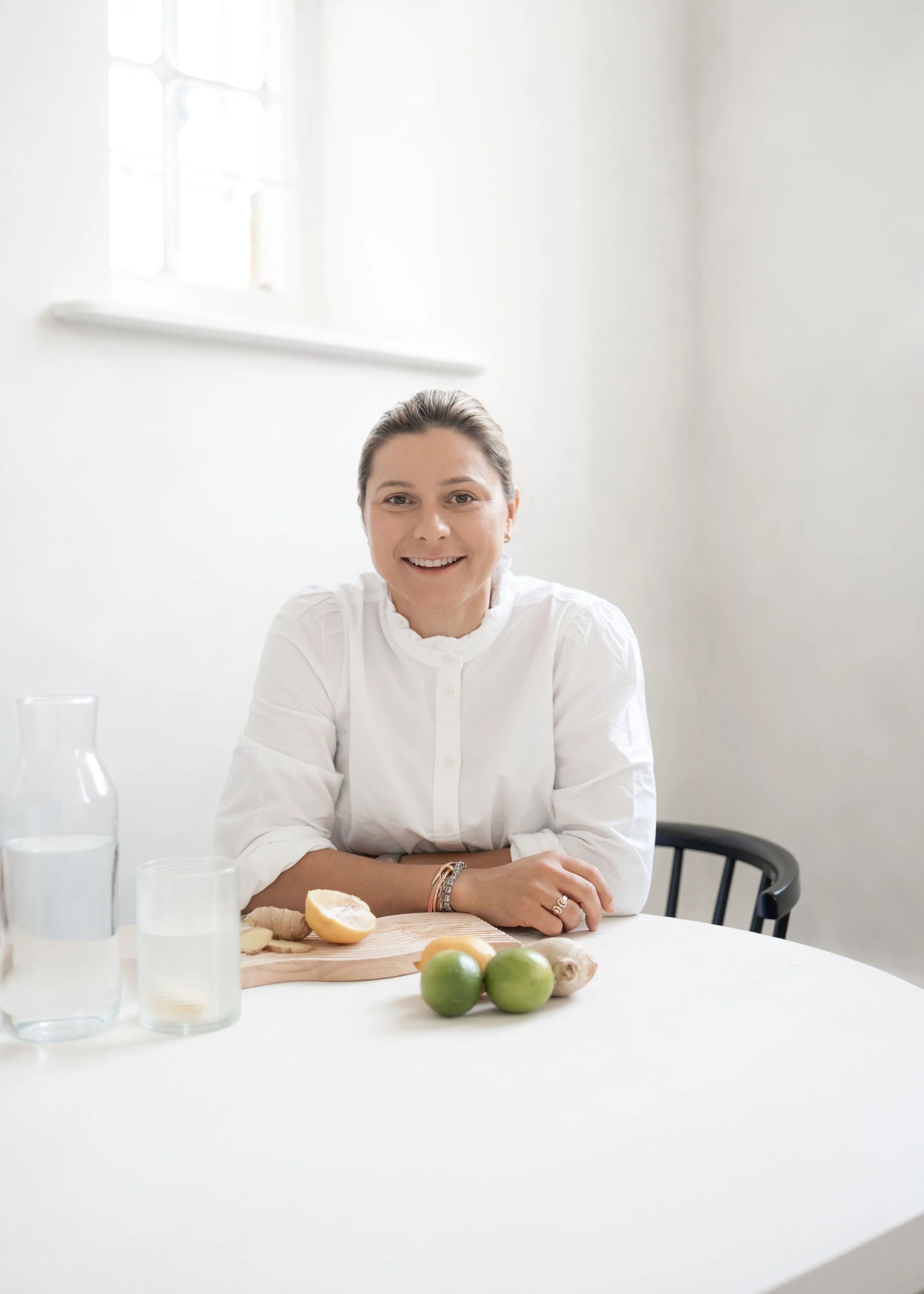 Victoria, certified Health Coach, Reiki Master and founder of Well by Plum, sitting at a white table with lemon, lime, and ginger - representing natural health, balance, and wellbeing.