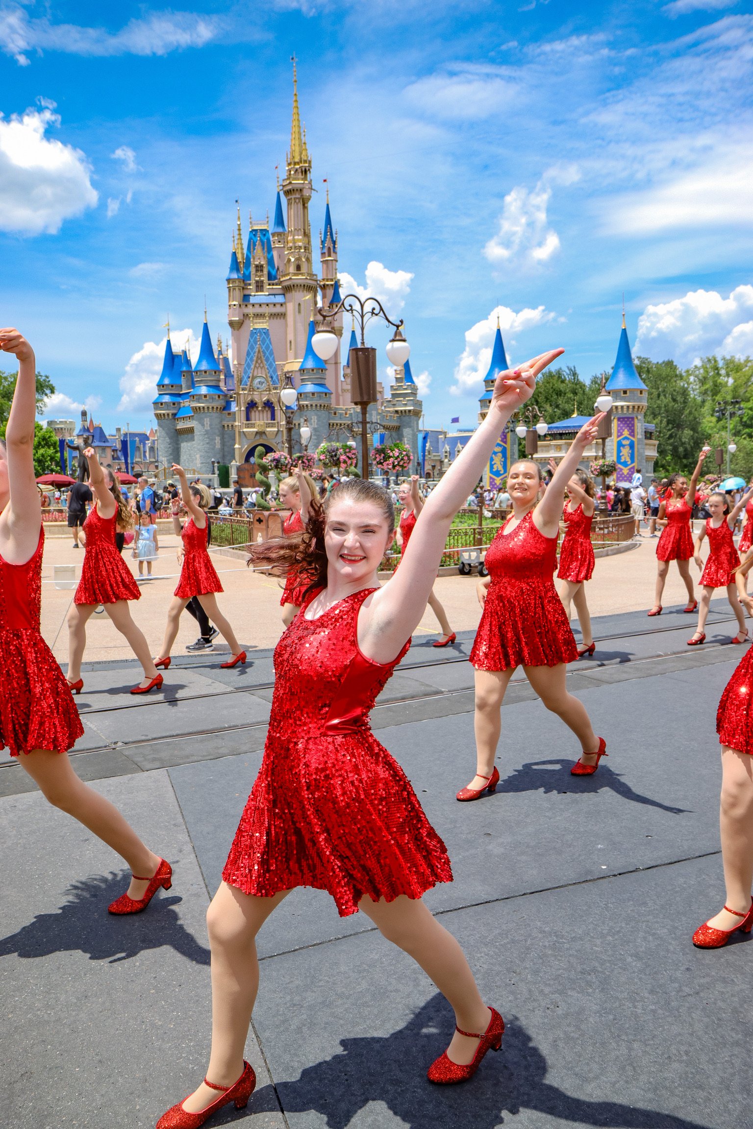 A group of women in red dresses dancing in front of Disneyland castle on a sunny day.