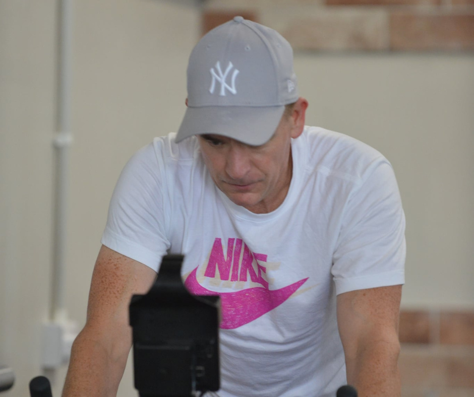 A man wearing a gray New York Yankees cap and a white Nike t-shirt is looking down, possibly at a workout machine or equipment.