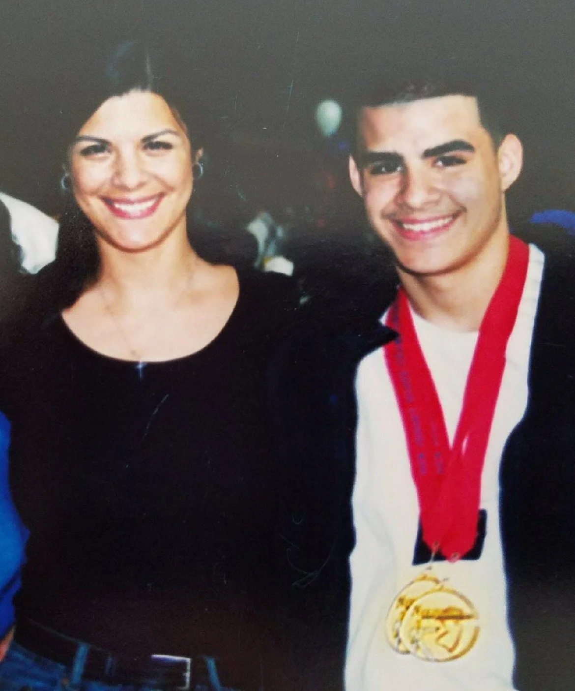 A woman and a young man are smiling at the camera, with the young man wearing a medal around his neck.