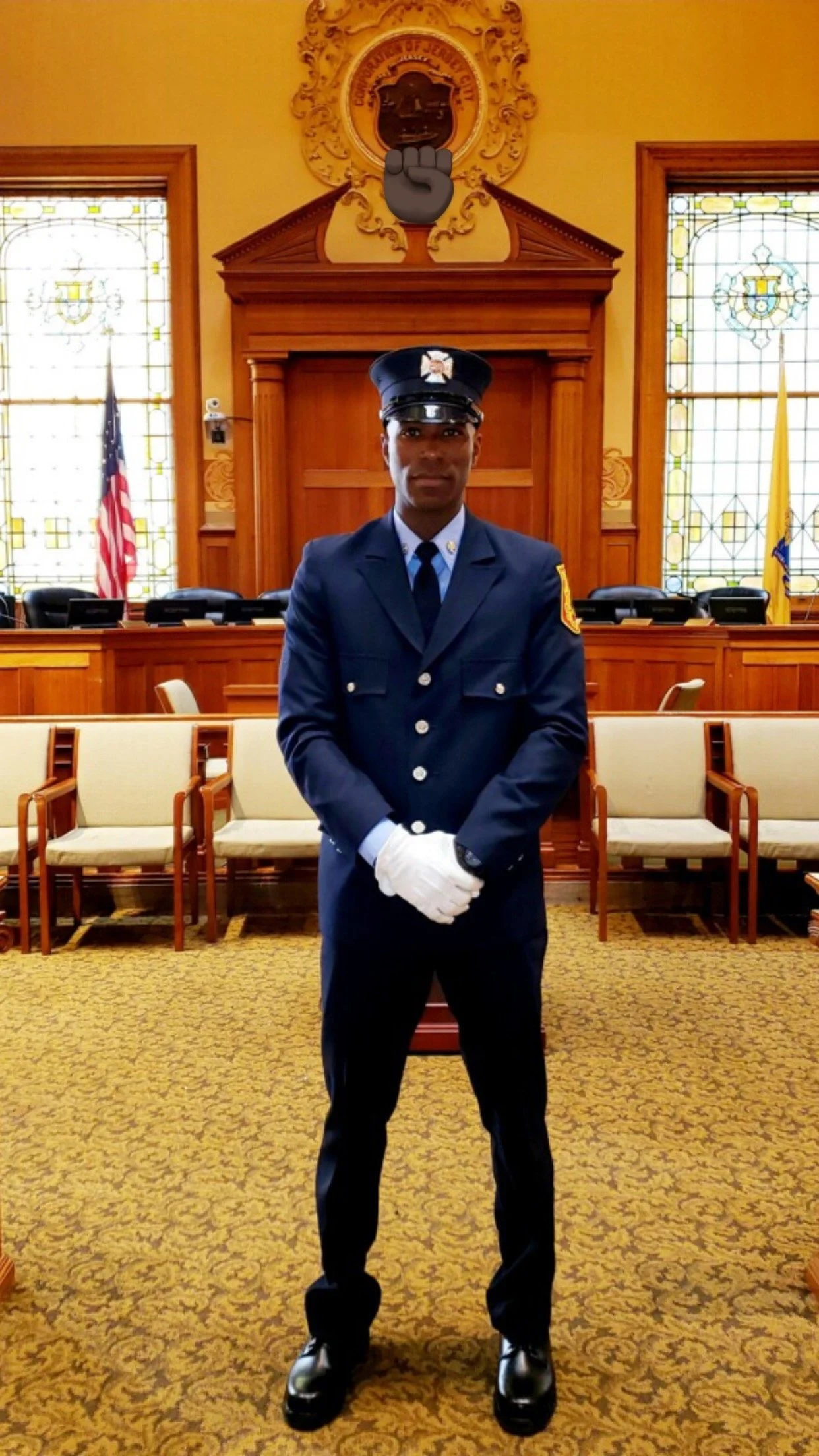 A police officer in uniform standing in a court room with wood paneling, flags, and stained glass windows.