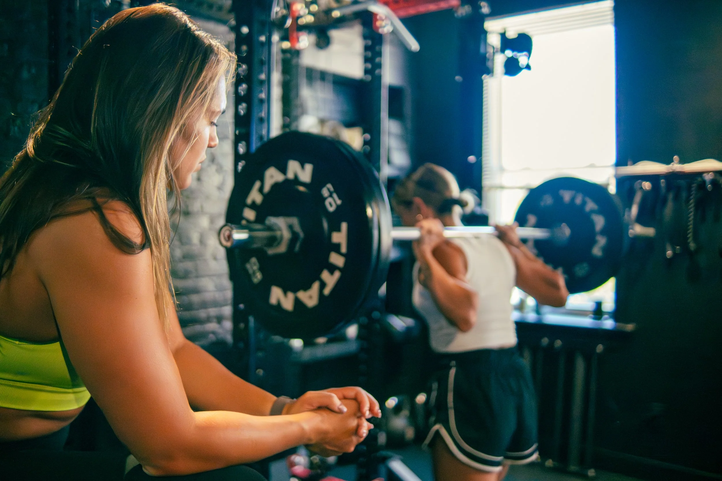 A woman holding a playful dog while a man lifting a kettlebell in a gym with brick walls.