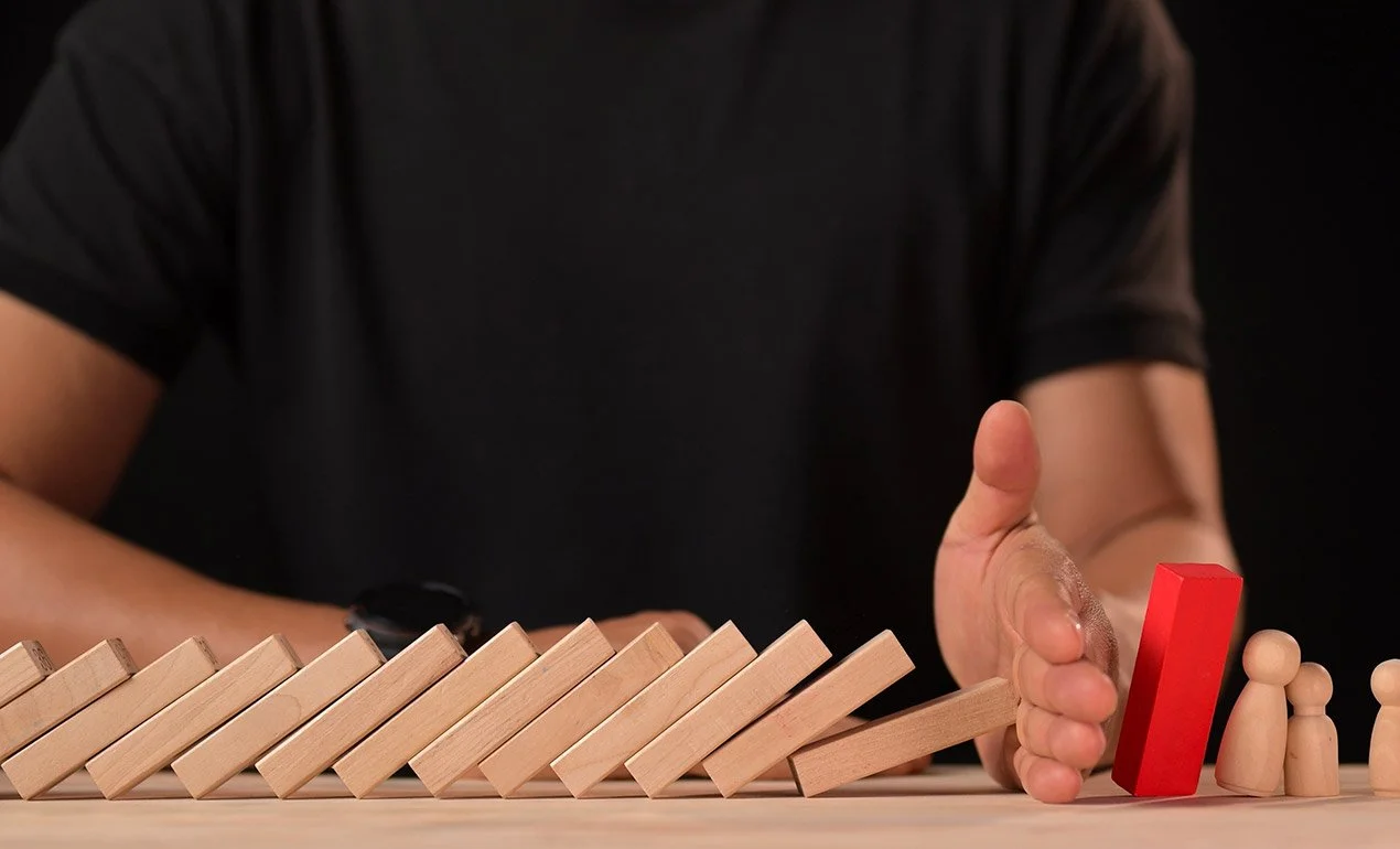 a hand stops a falling line of dominoes before the falling dominoes can strike the important