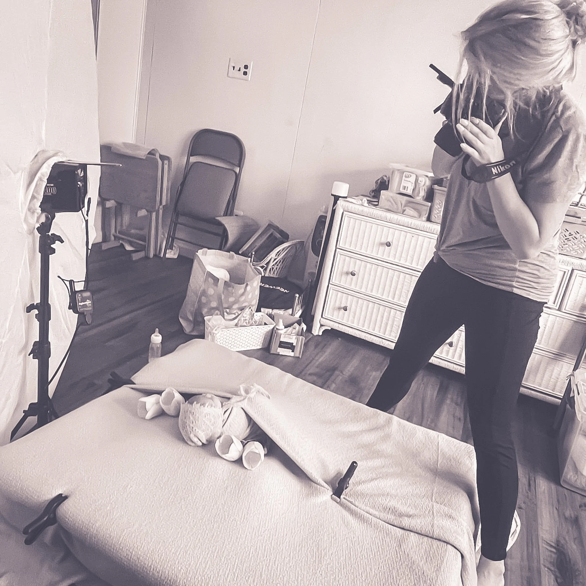 Black and white image of a photographer with her camera in hand and she is photographing a newborn baby.