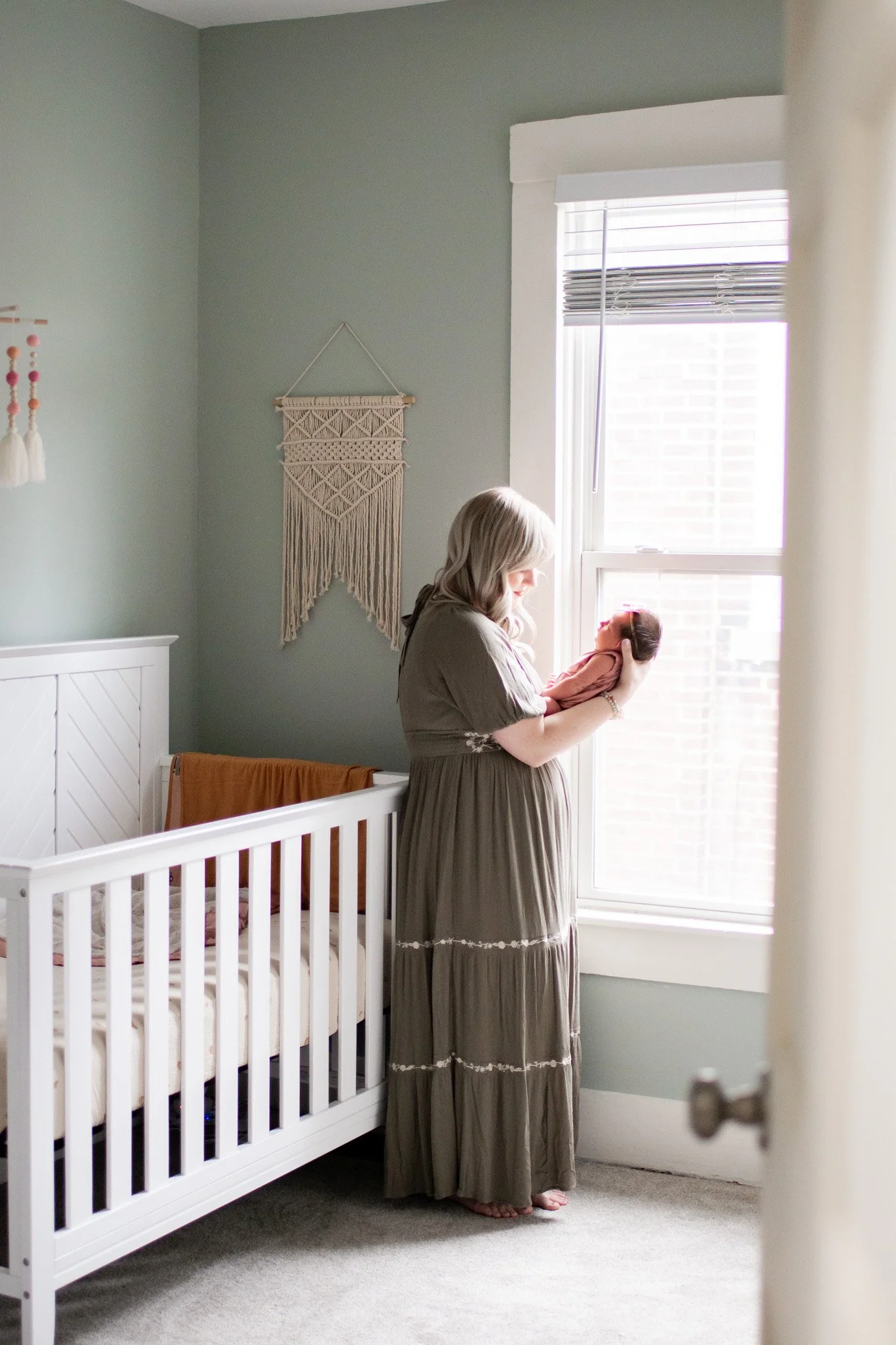 Mom holding newborn baby by the window in the nursery