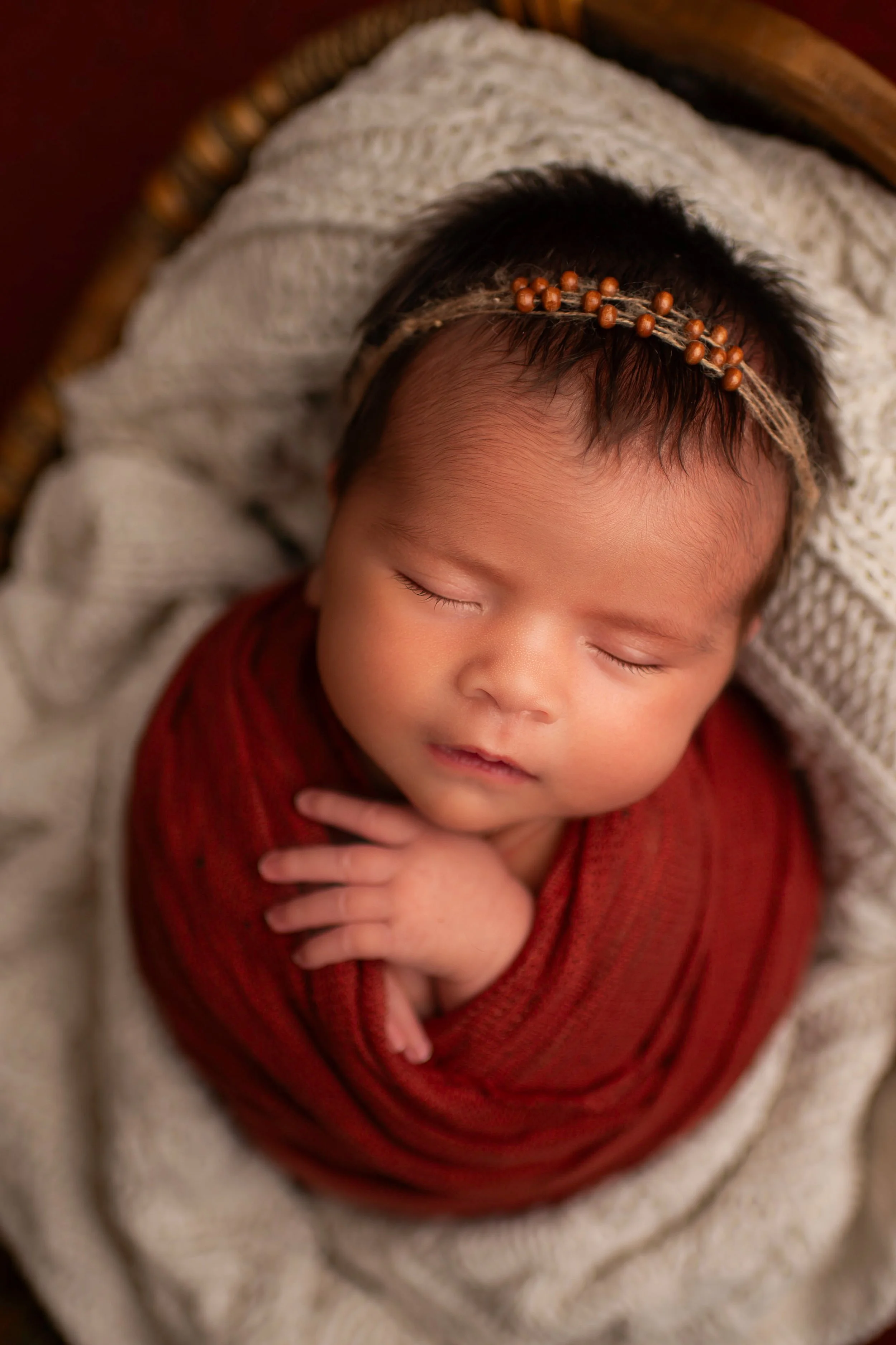 Newborn baby girl asleep in a basket and wrapped in a burnt orange swaddle