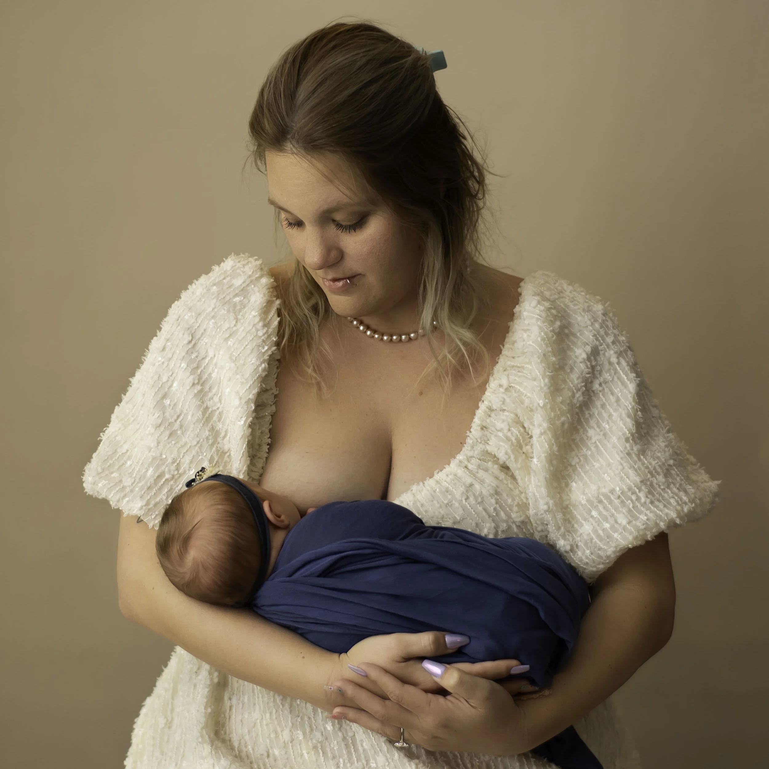 Mom nursing a newborn baby on a neutral backdrop