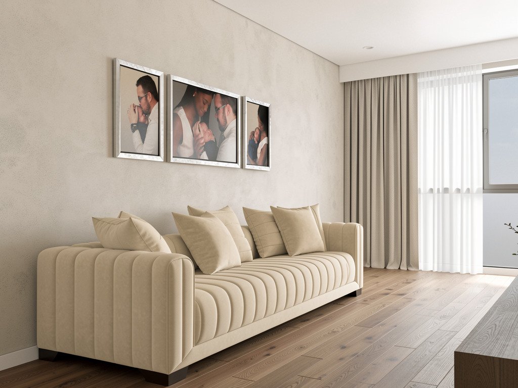Modern living room with a cream sofa and beige cushions, framed artwork on the wall, sheer curtains, and sunlight coming through a window.