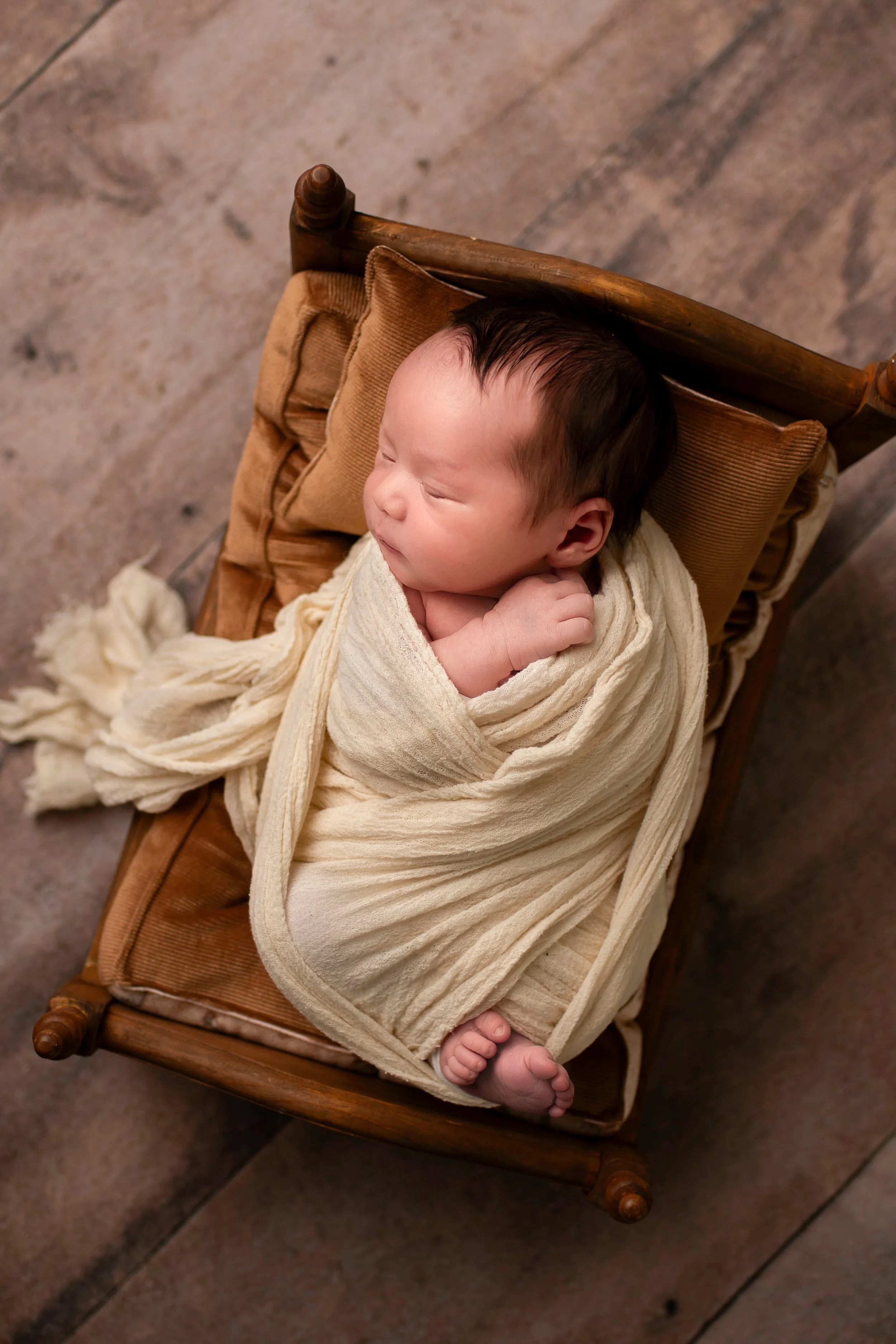 Baby boy swaddled in a neutral wrap on a tiny newborn size bed