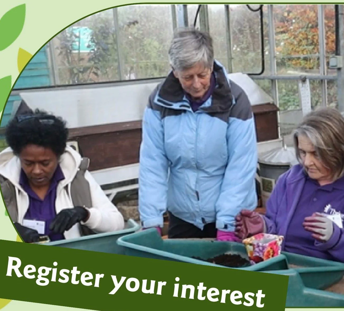 Three women sitting at a work bench in a green house planting seeds