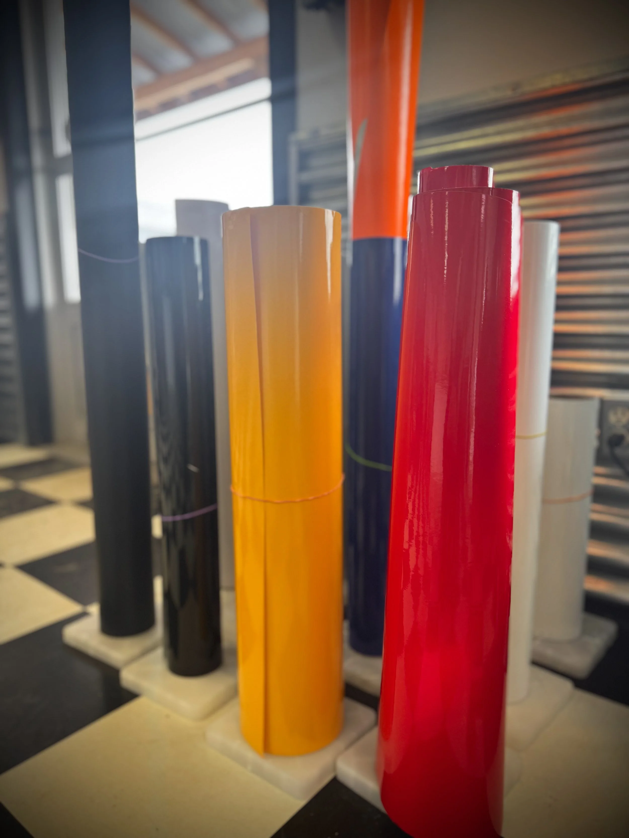 A fleet of four construction and service vehicles with matching company logos and branding traveling along a rural road at sunset, including a white pickup truck, a white semi-truck, a red dump truck, and a tracked excavator.