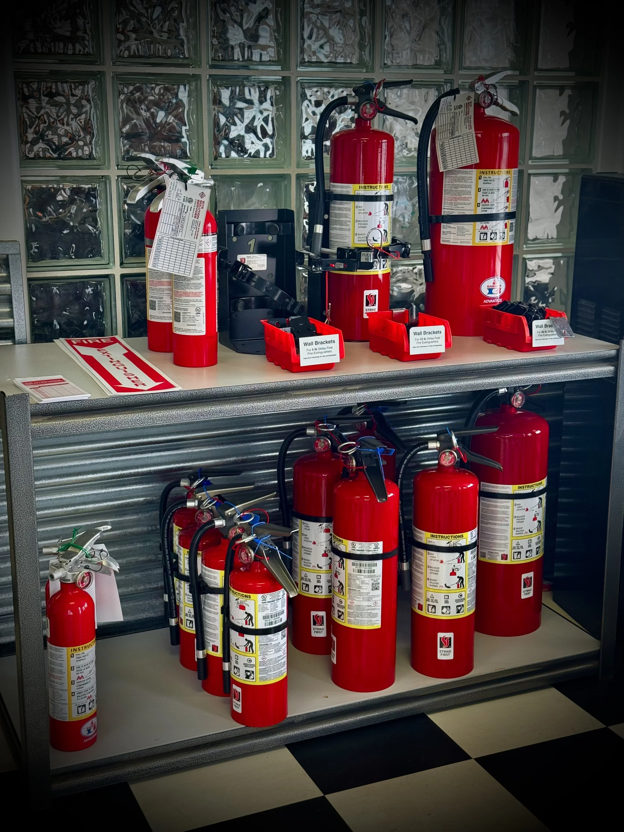 A black emergency response trailer with logos, safety equipment including fire extinguishers, traffic cones, a high visibility jacket, and a spotlight, set against a mountain landscape with trees and blue sky.