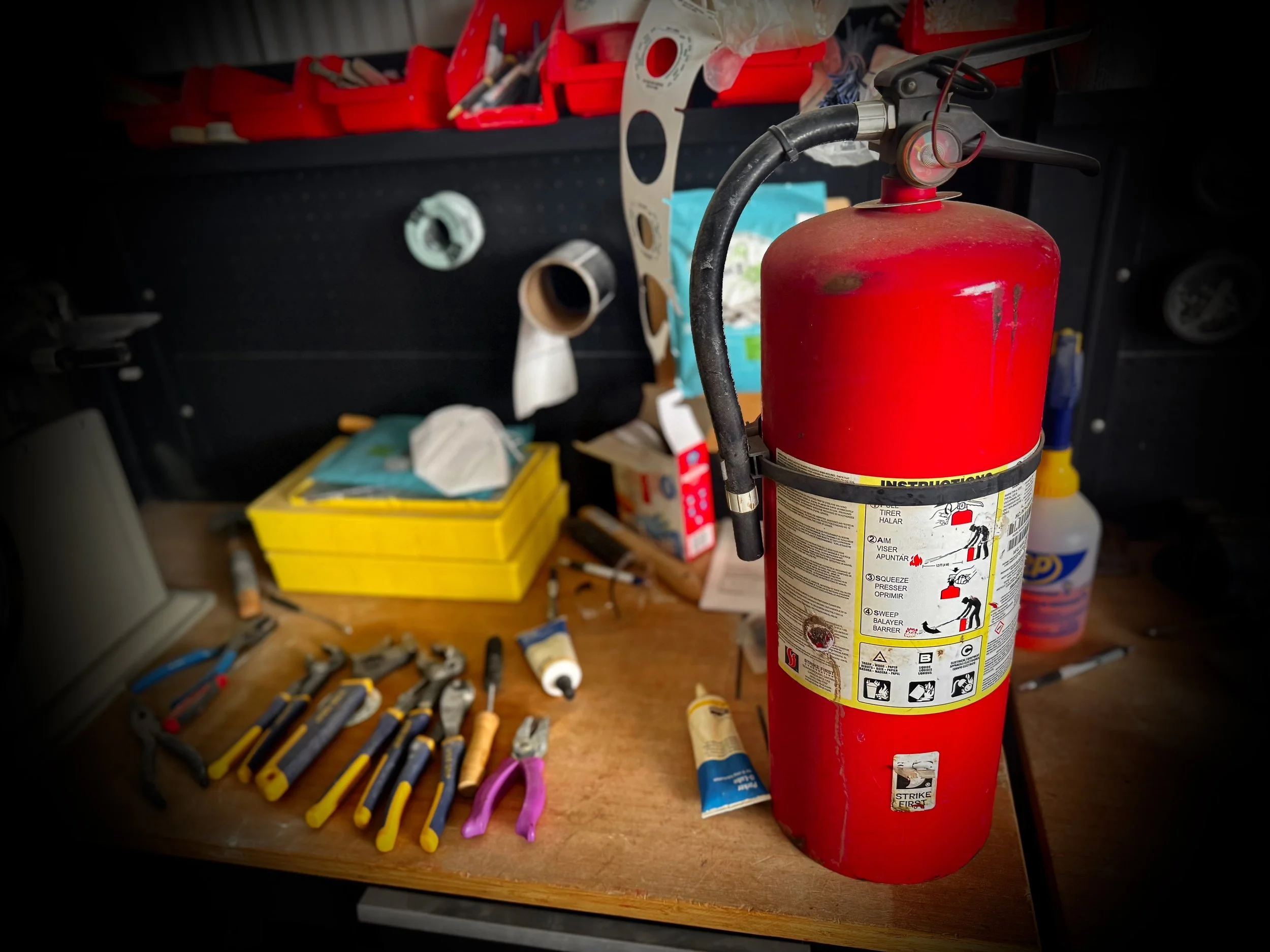 Red fire extinguisher mounted on a safety cabinet with safety signs, including fire hazard, warning, protective equipment, and safety instructions, outdoors.