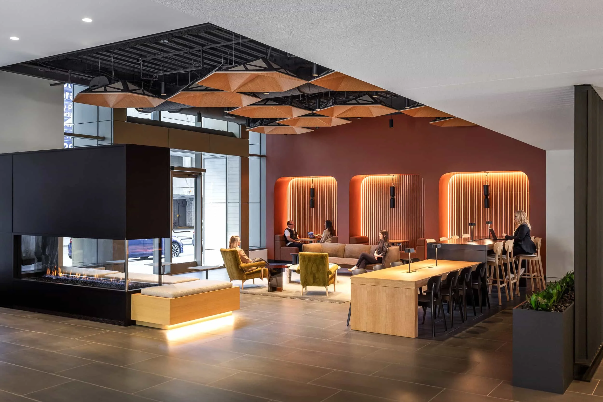 Modern hotel lobby with seating area, wall-mounted lighting, fireplace, and large glass windows.