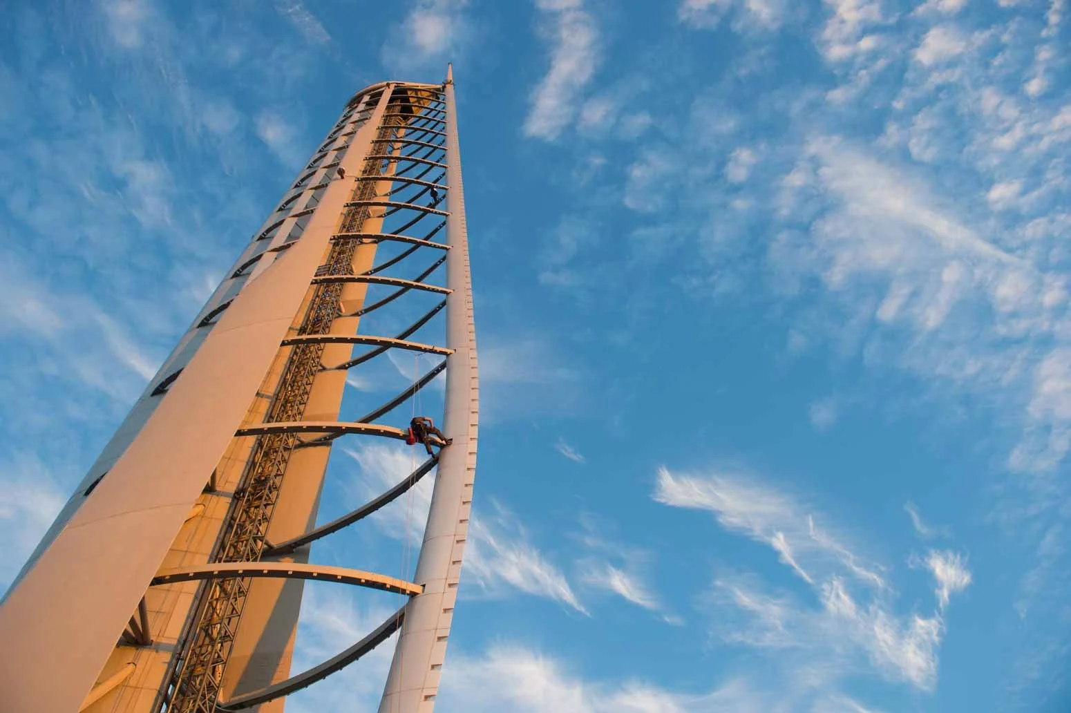 A tall roller coaster with a vertical drop against a blue sky with scattered clouds.