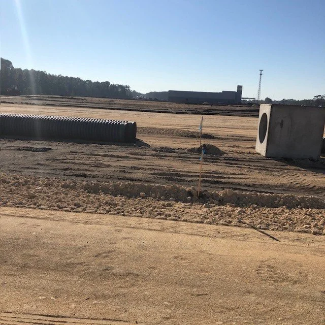A construction site with a large corrugated pipe, a concrete cylindrical structure, and a pole with marking flags, under a clear sky.