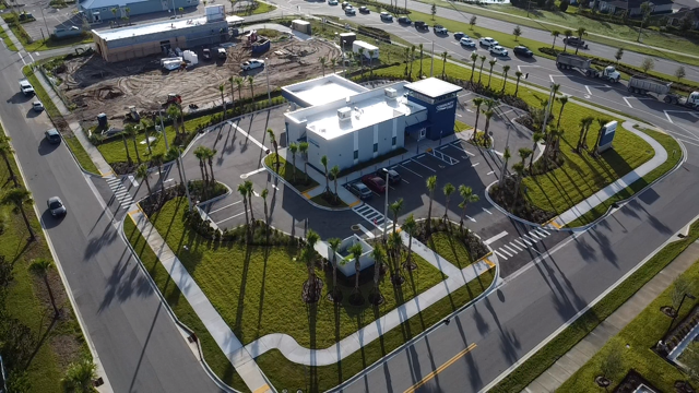 Aerial view of a modern white building surrounded by a landscaped parking lot with palm trees and walking paths.