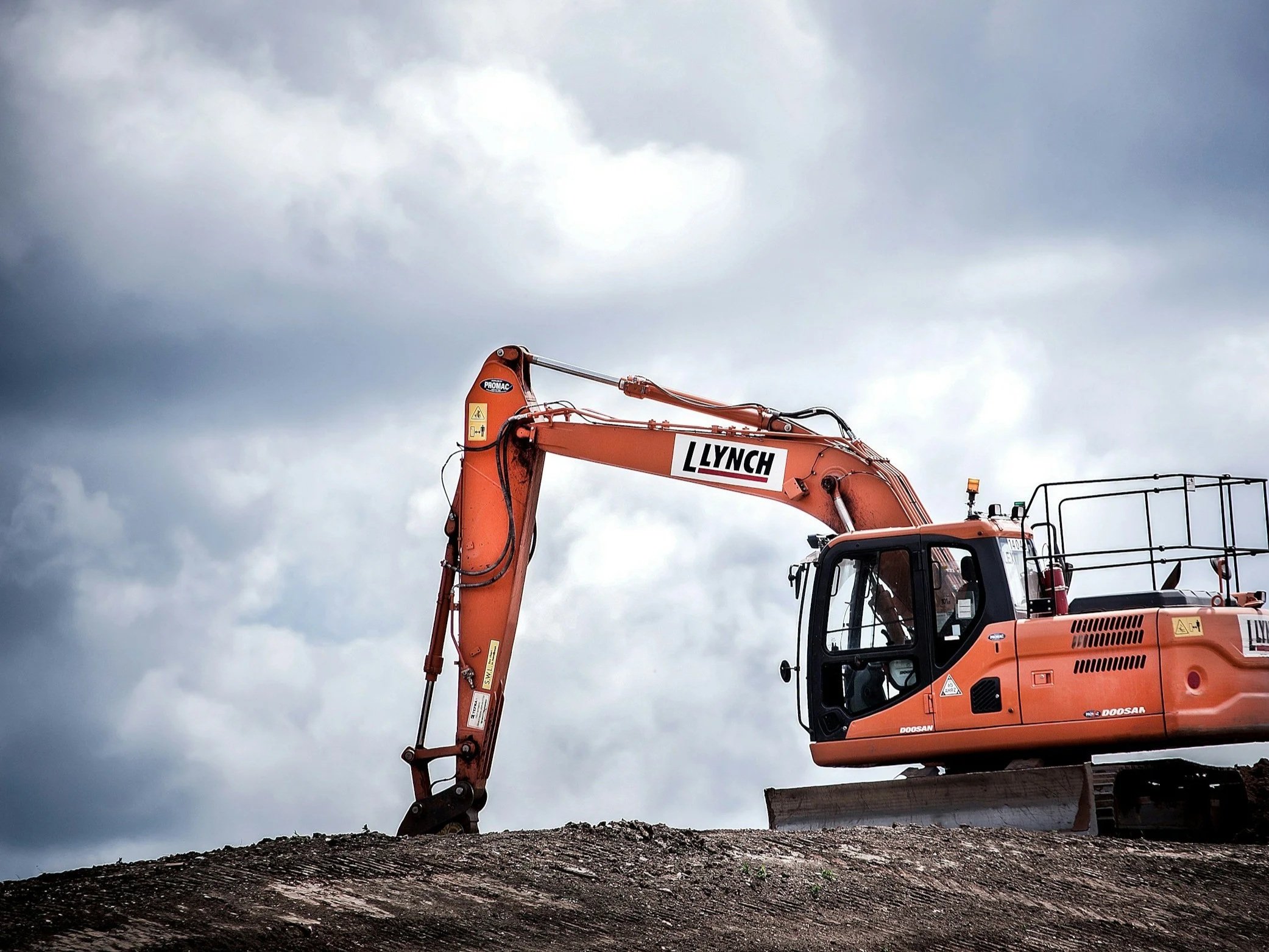 An orange excavator on a construction site with a cloudy sky in the background.