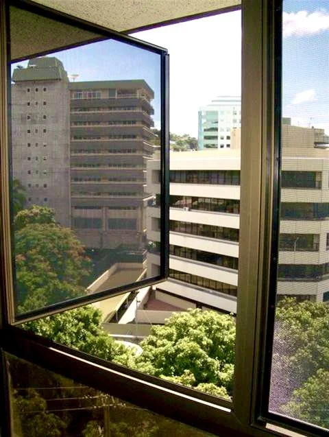 Open window overlooking modern office buildings and green trees outside.