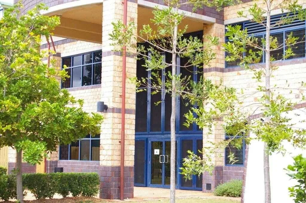 Exterior view of a modern brick building with large glass doors and windows, surrounded by trees and shrubs.