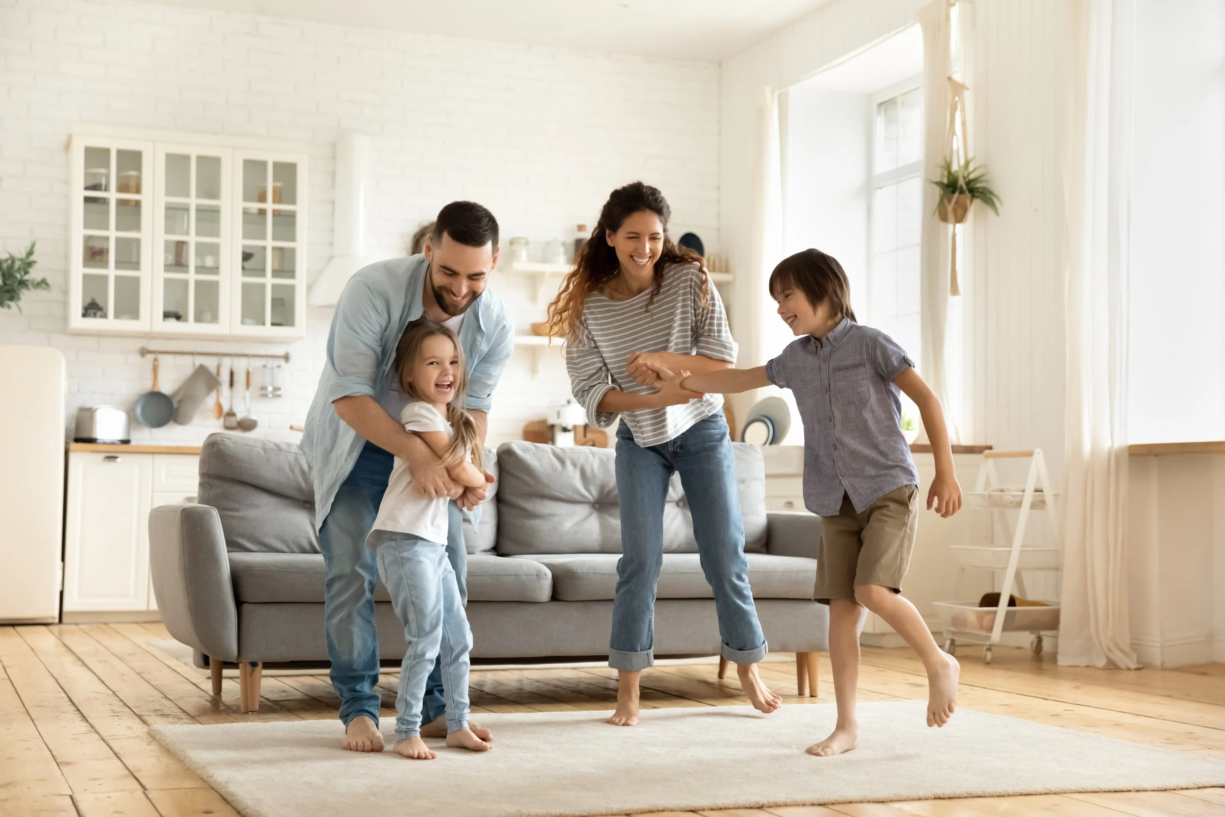 A family of four playing and laughing together in a bright, cozy living room.