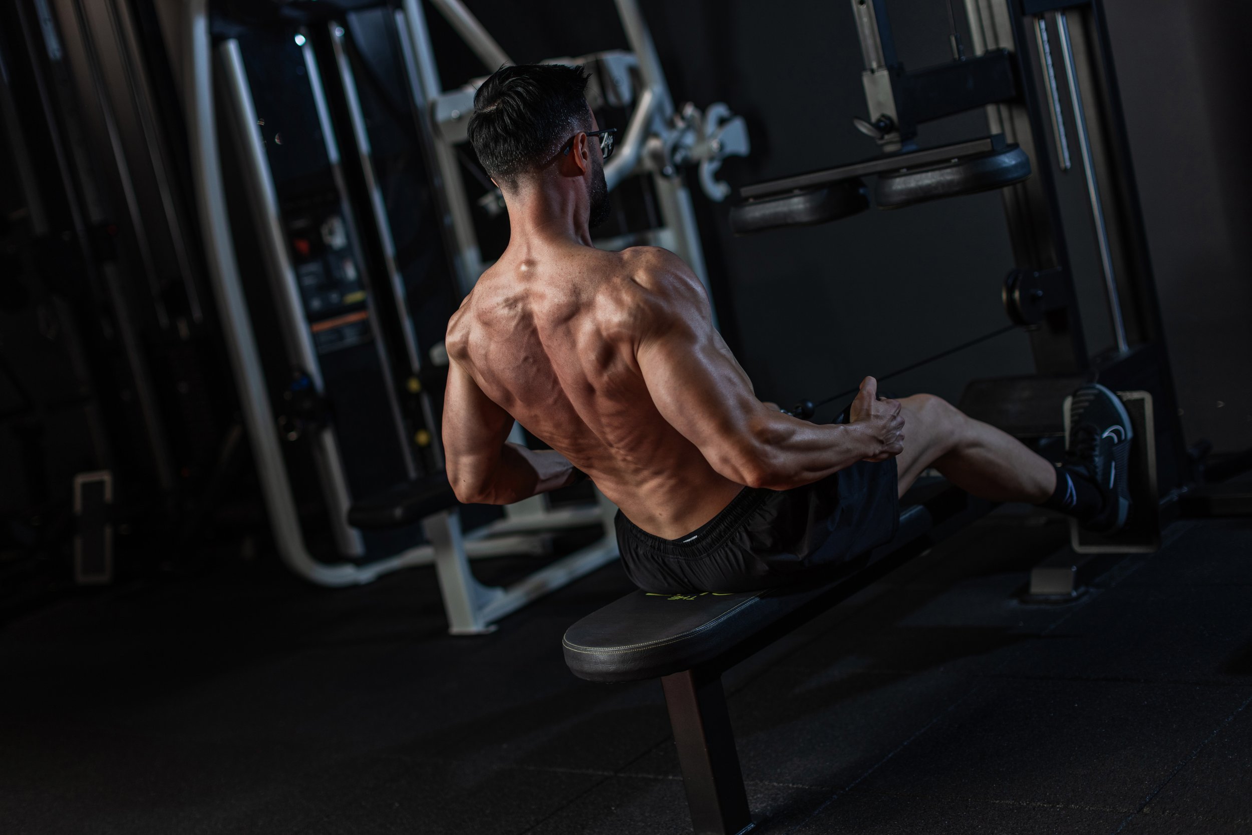 A muscular man working out on a seated rowing machine in a gym.