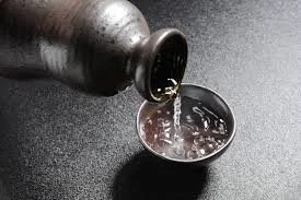 Black bottle pouring a clear liquid into a small container on a dark surface.