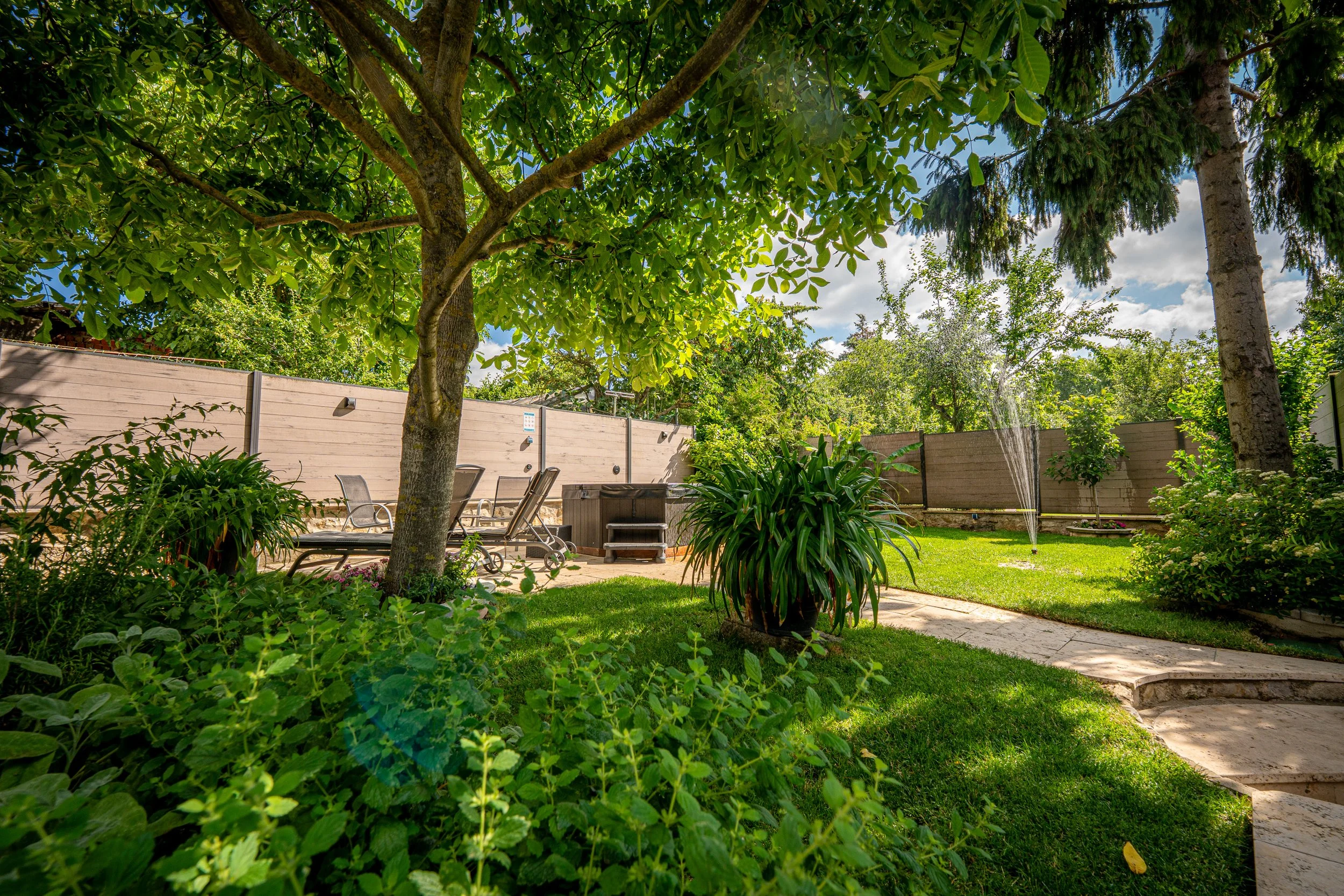 Garten mit Bäumen, Rasen, Gartenmöbeln und Wasser sprüht