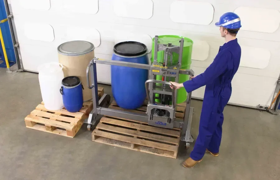 Operator is lifting a green 55 gallon steel drum with a stainless steel drum lifter that is straddling the pallet
