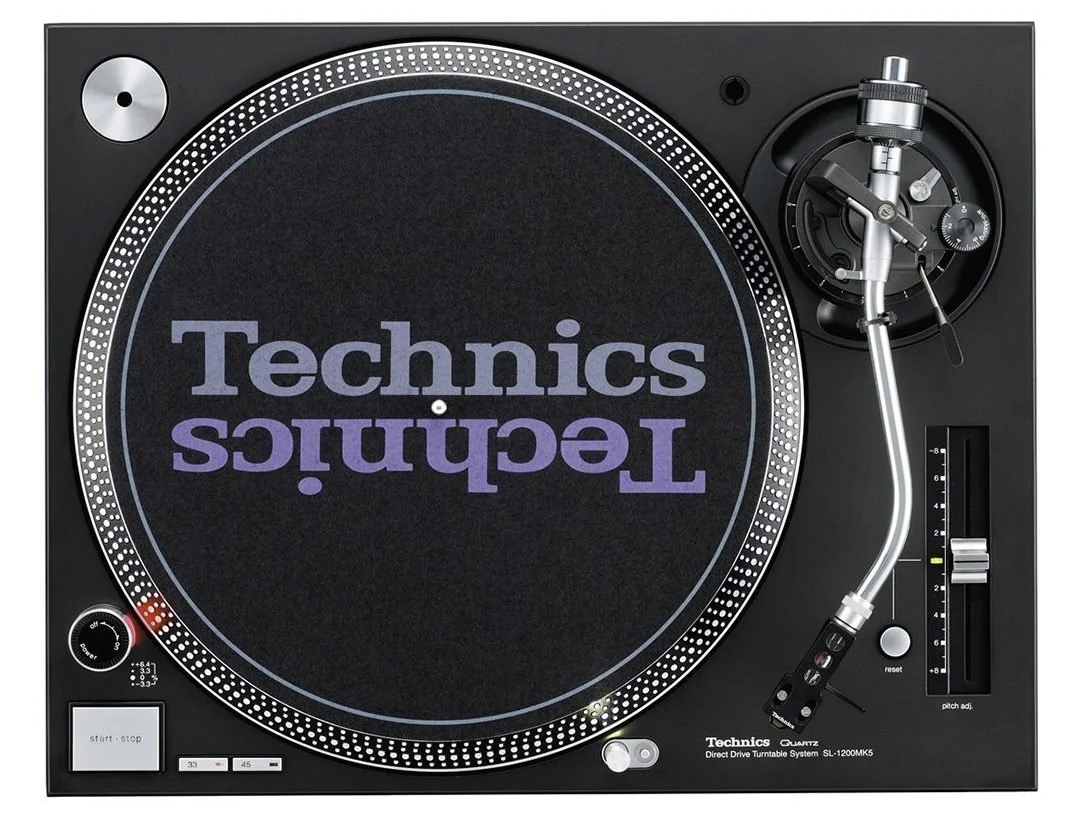 A Technics turntable with a black surface, with the Technics logo in purple and gray on the spinning platter, and various controls and the tonearm visible.