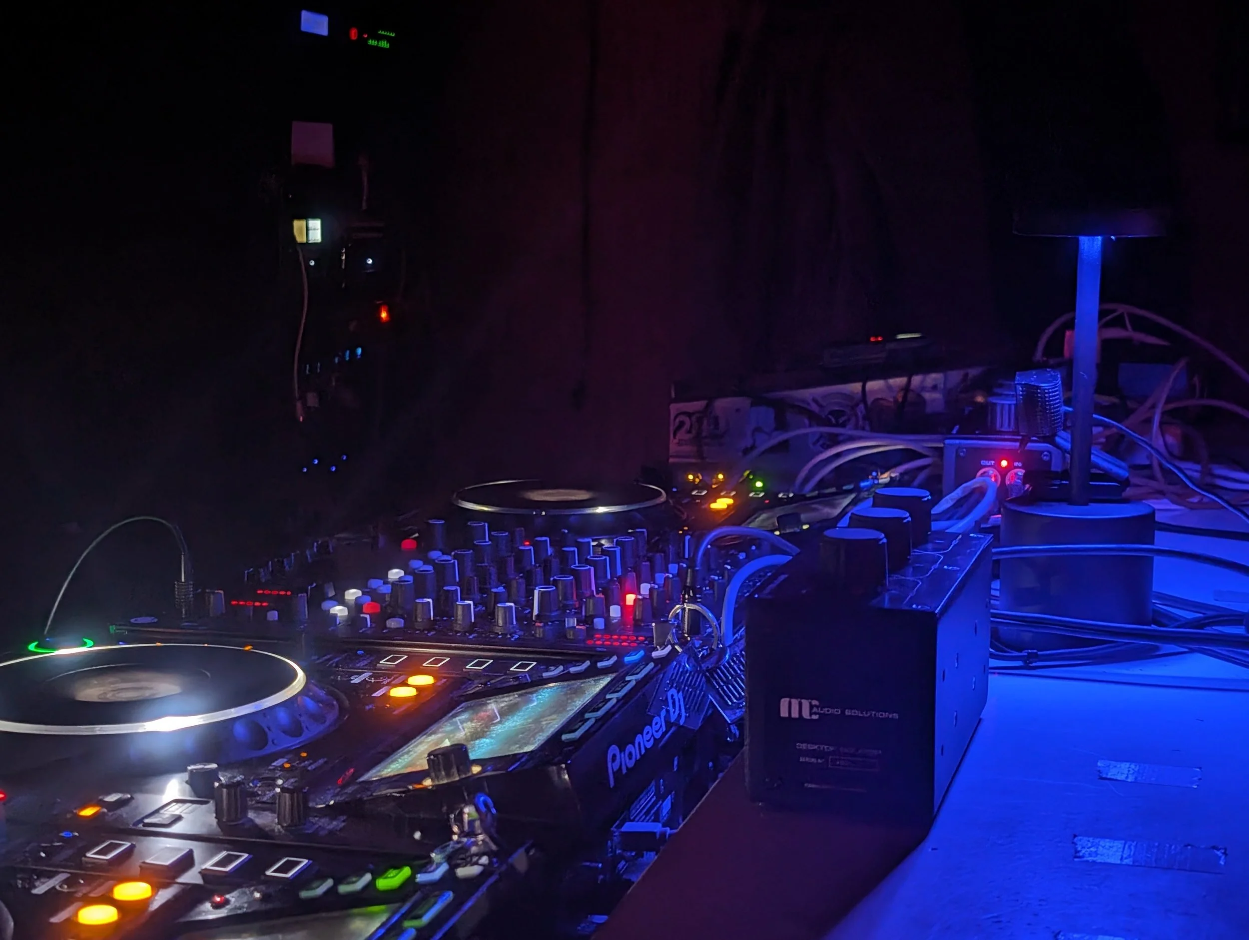 Close-up of DJ equipment with a hand adjusting settings, two Pioneer DJ controllers with colorful displays and buttons, set up for music mixing.