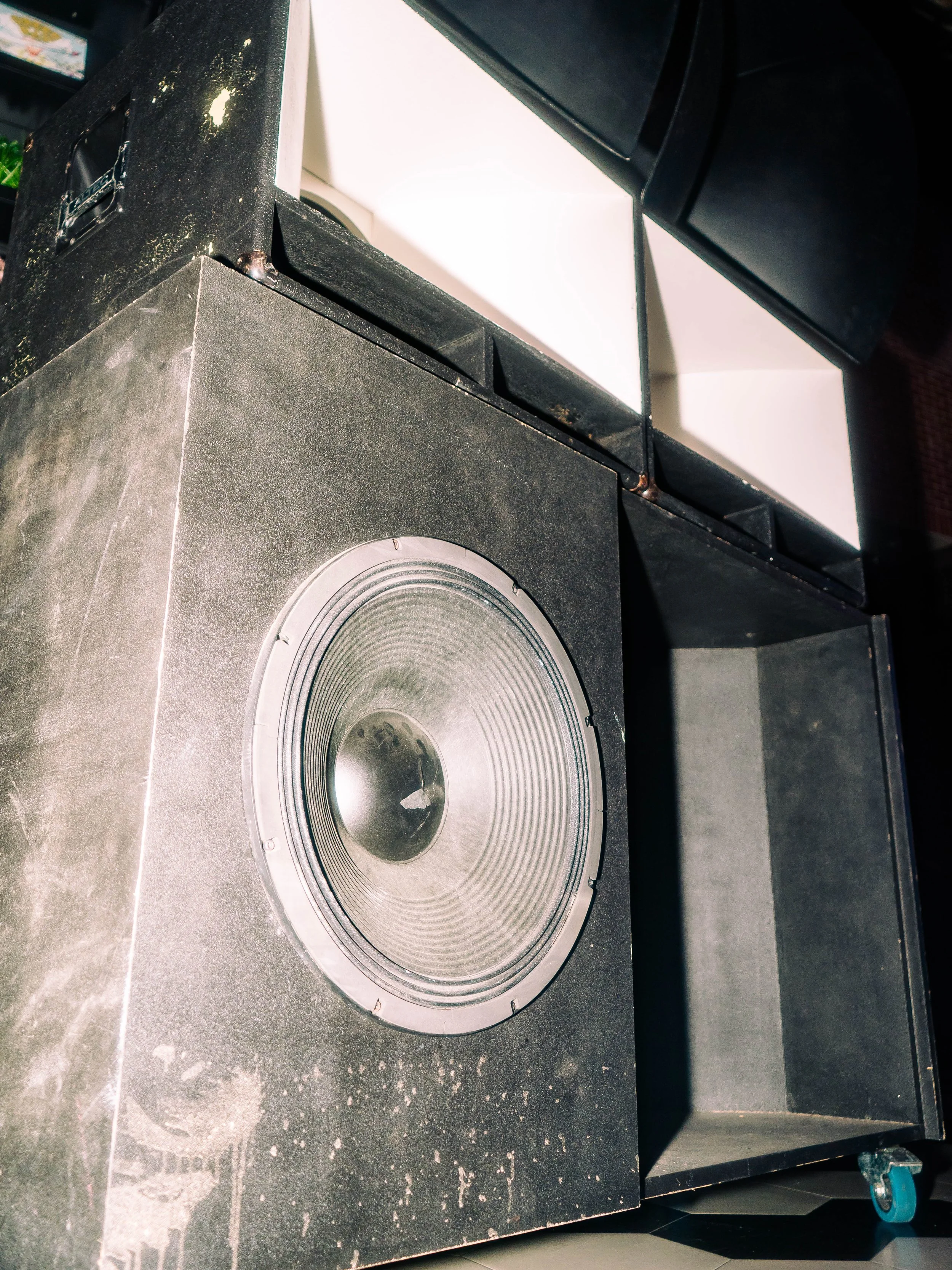 Large black speaker with a circular woofer, adjacent to a black enclosure, with some white and black rectangular components on top
