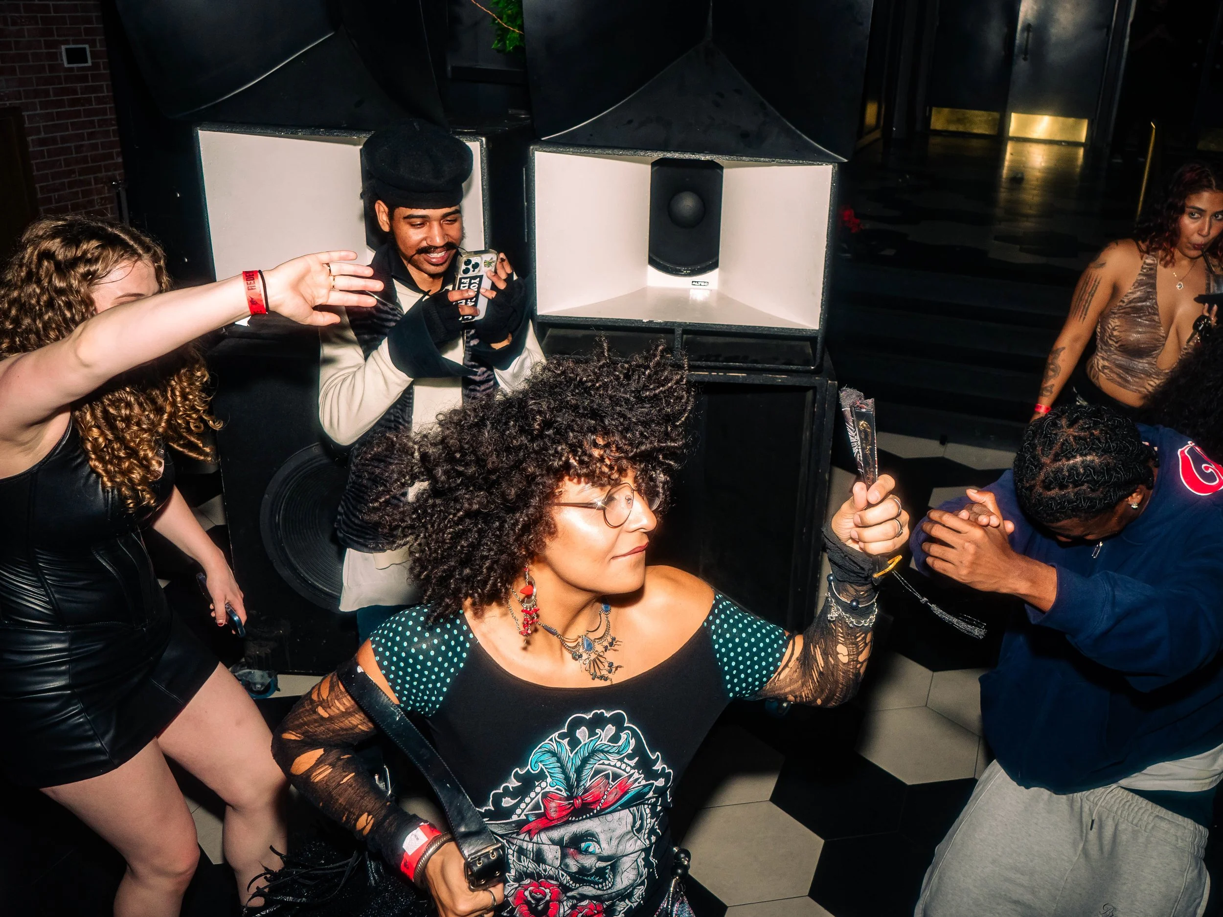 Group of people dancing and socializing at a party with a DJ booth in the background.