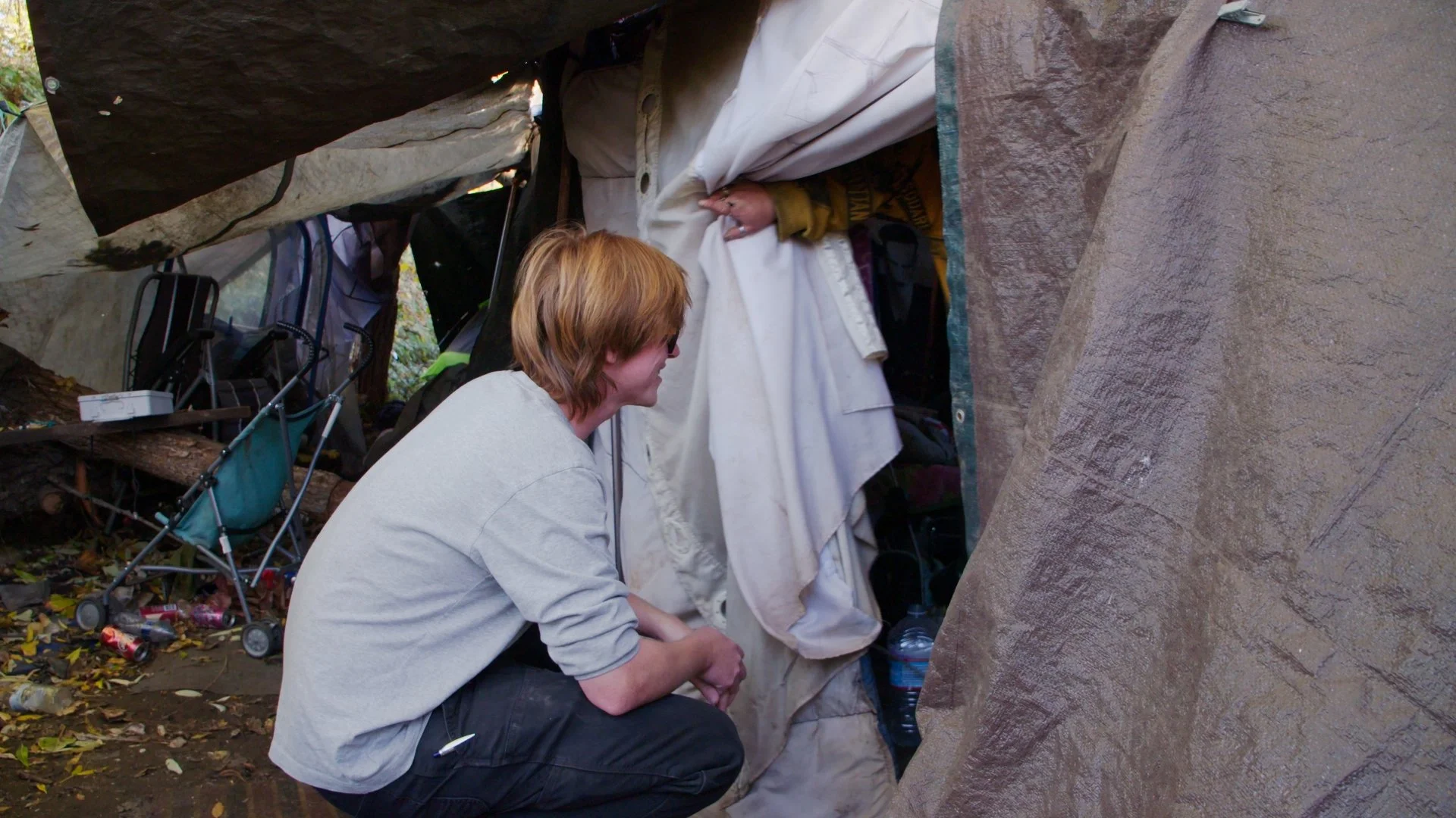 A provider from WINGS with short hair squats outside a makeshift shelter, talking with an unhoused person.