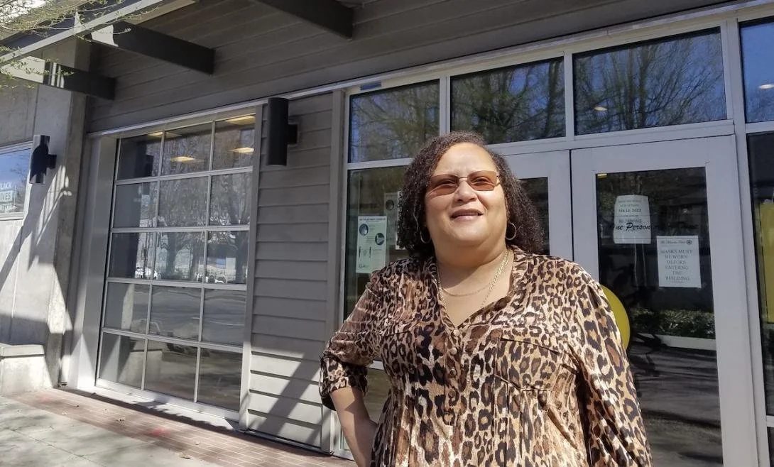Executive Director of Miracles Club stands outside their building in a leopard print top stands with one hand on a hip.