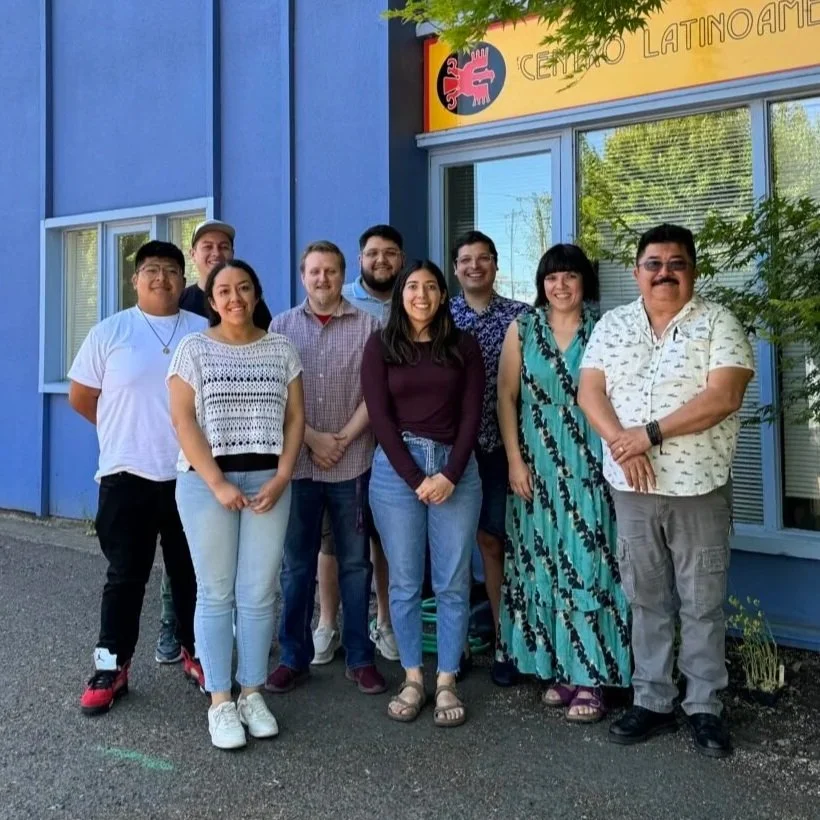 Group of nine people standing outside a blue building with a yellow sign that reads 'Centro Latinoamericano' and logo, smiling at the camera.