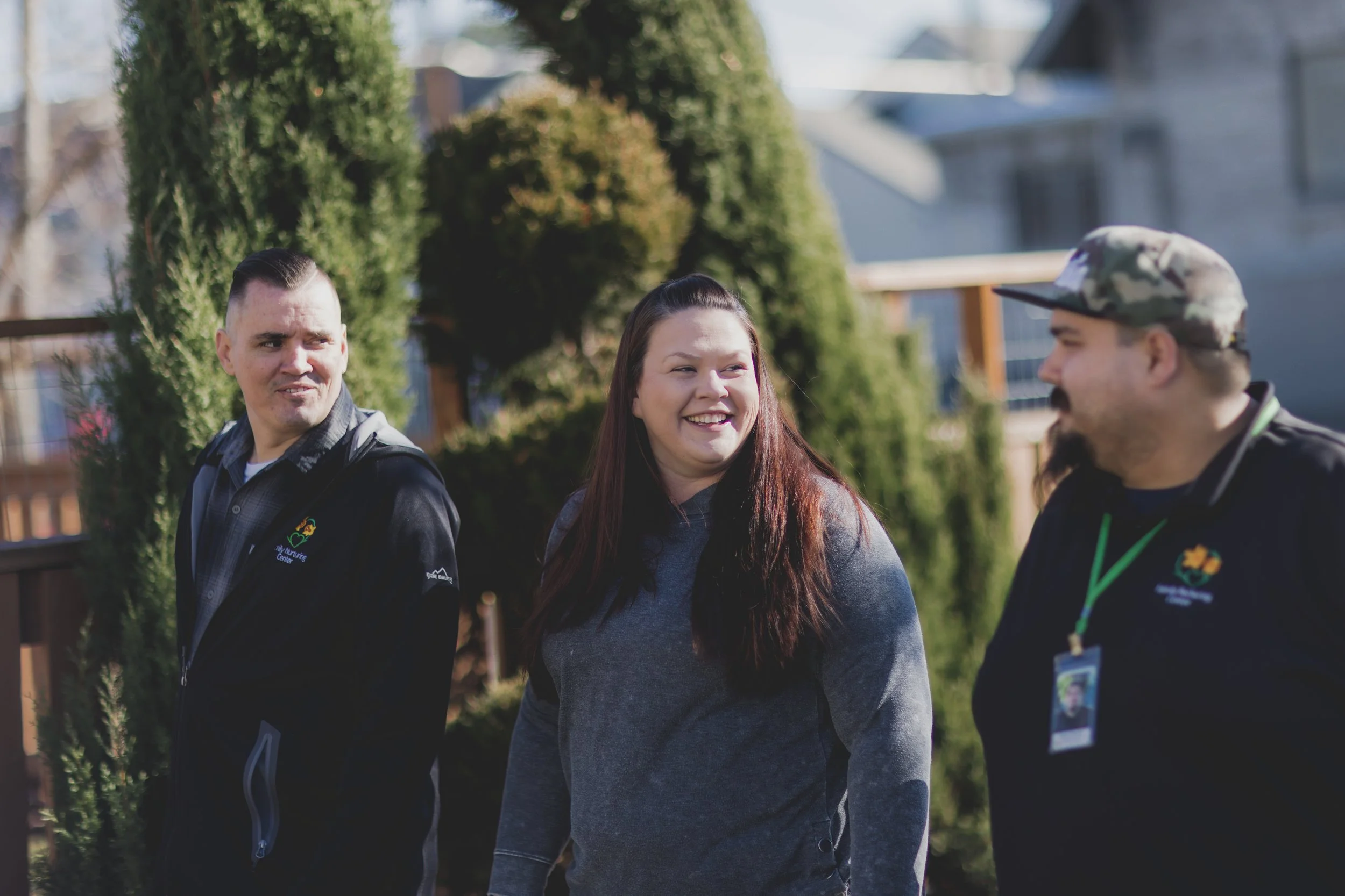 Three providers at Family Nurturing Center walking outdoors, smiling and talking. Two men and one woman, dressed casually, with trees and houses in the background.