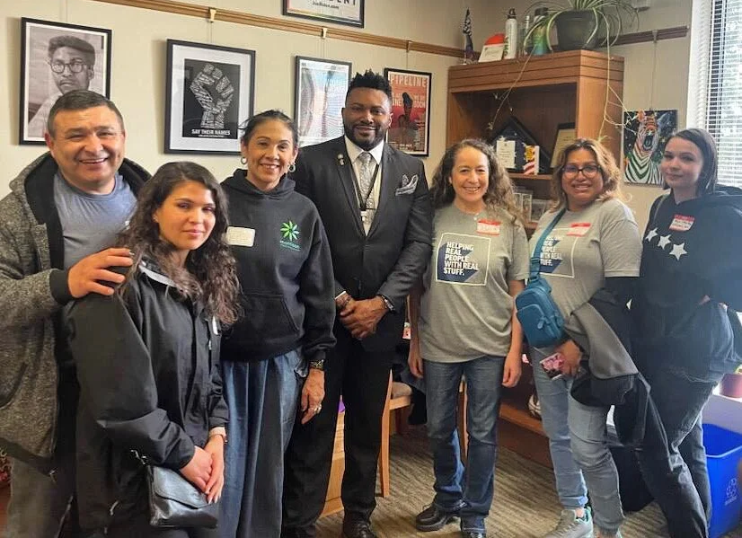 Group of seven HJRA advocates stand together indoors, smiling, with framed pictures on the wall behind them.