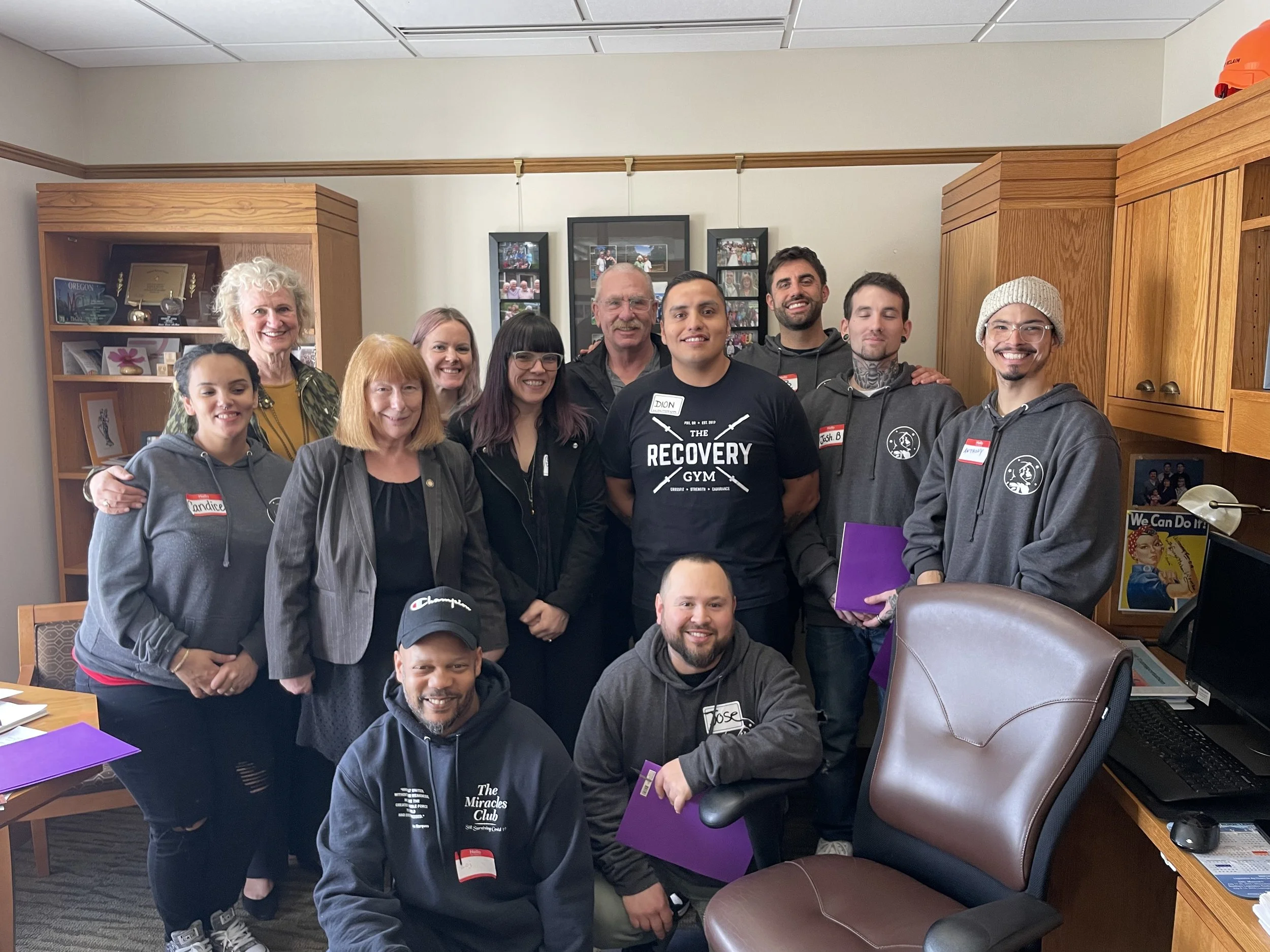 Group of 13 HJRA advocates gathered in an office, smiling for the camera, some holding purple folders.
