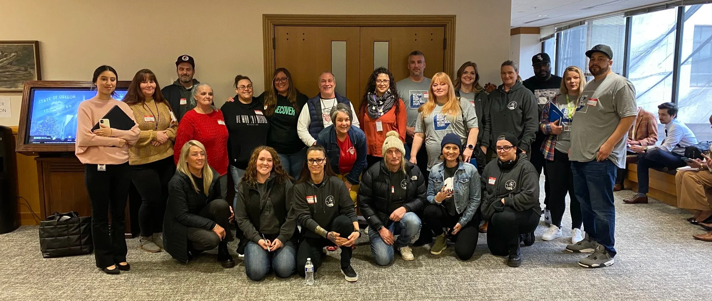 A group of diverse HJRA advocates pose for a photo indoors, standing and kneeling in front of wooden double doors, with windows on the right.