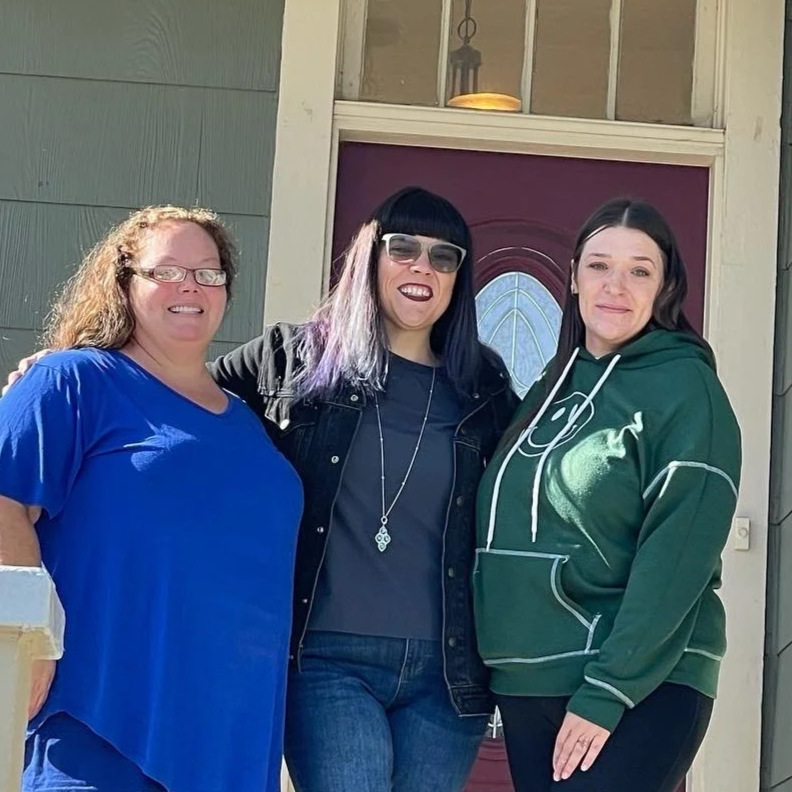 Three women standing together outside of WINGS house, smiling at the camera.