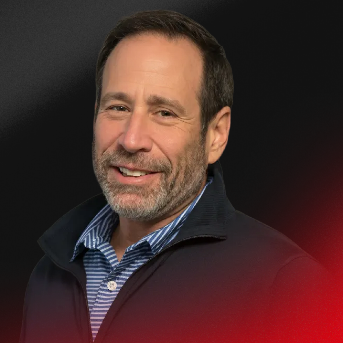 A middle-aged man with brown hair and a beard, smiling, wearing a blue striped shirt and a black jacket, against a dark background.
