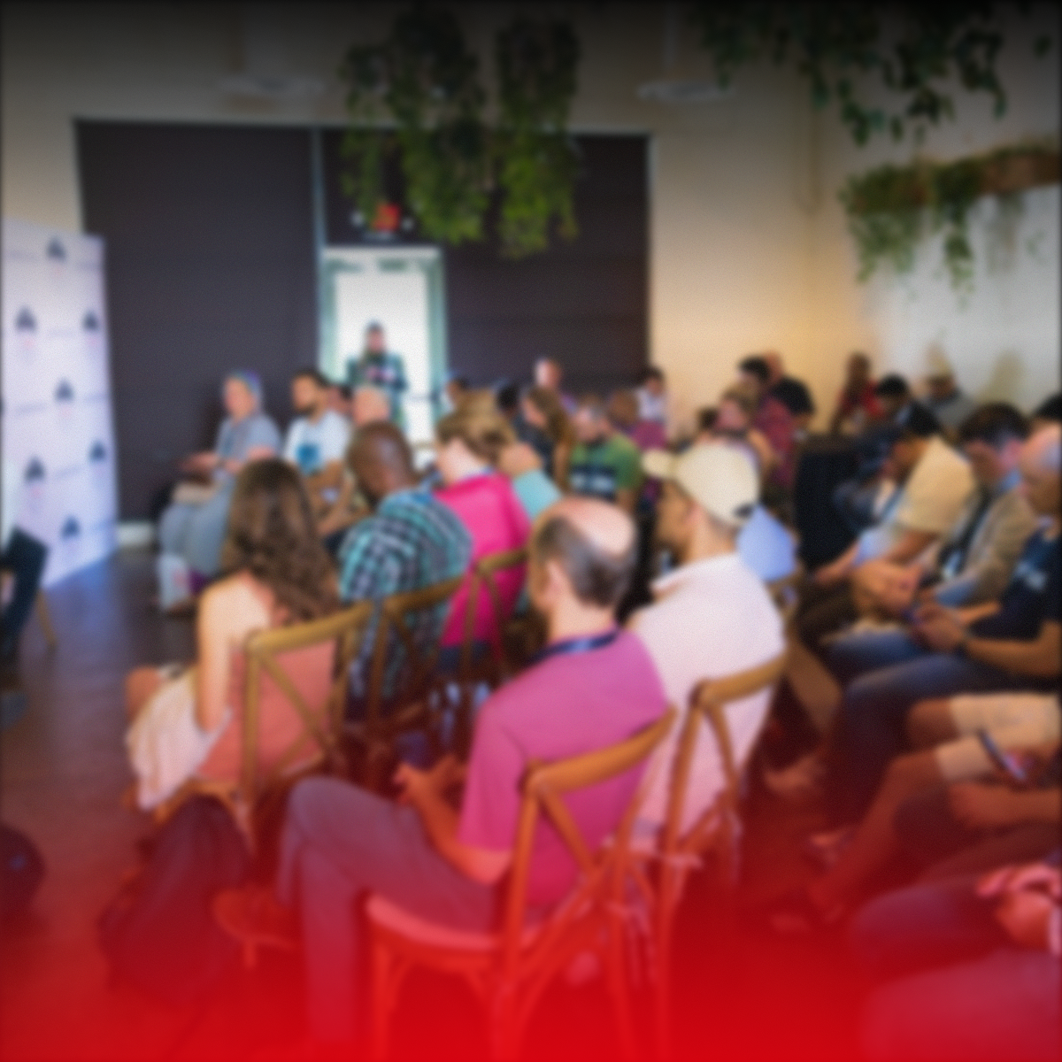 A group of people attending a presentation or conference in a room with some plants hanging from the ceiling.